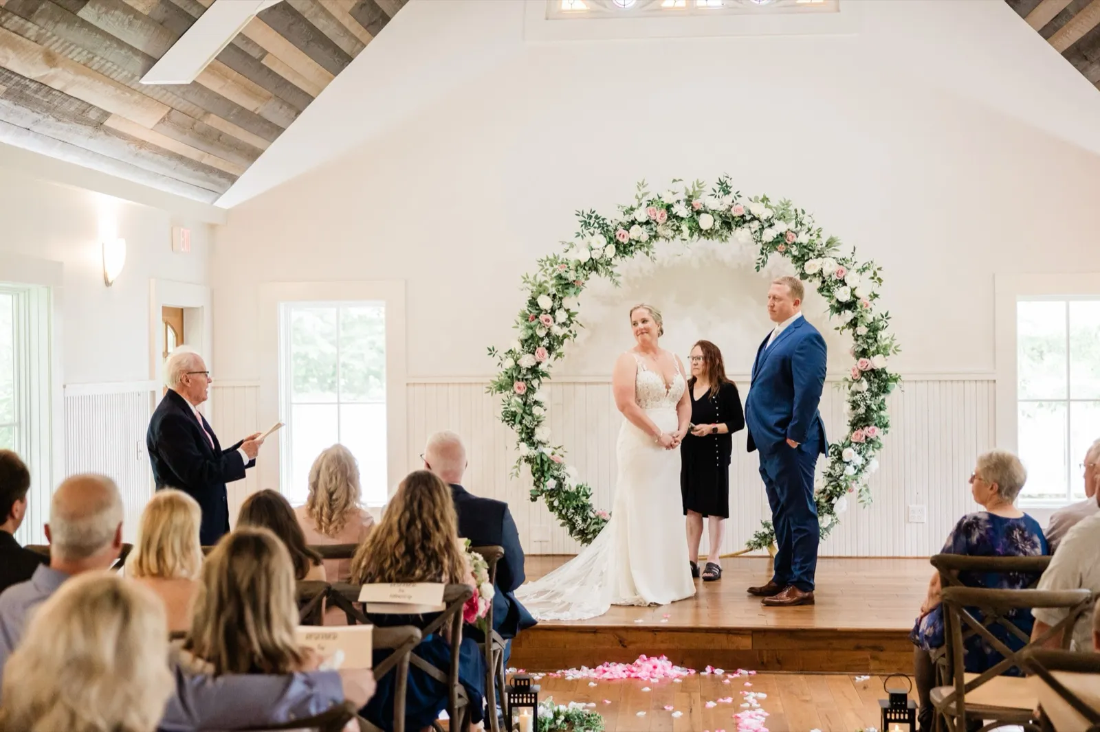 The couple stands at the circular floral arch with their officiant as seated guests look on — Tim Larsen Photography, Brainerd Lakes MN