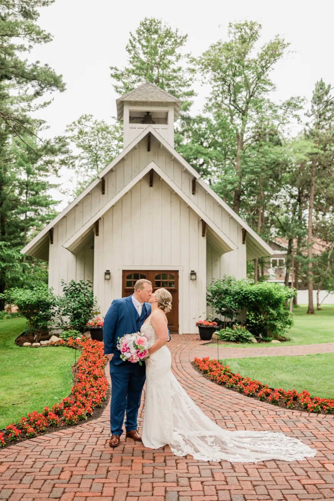 Lauren and Jeremy kiss on the red-brick walkway in front of The Chapel at Grand View Lodge, its bell tower against the pines — Tim Larsen Photography, Brainerd Lakes MN