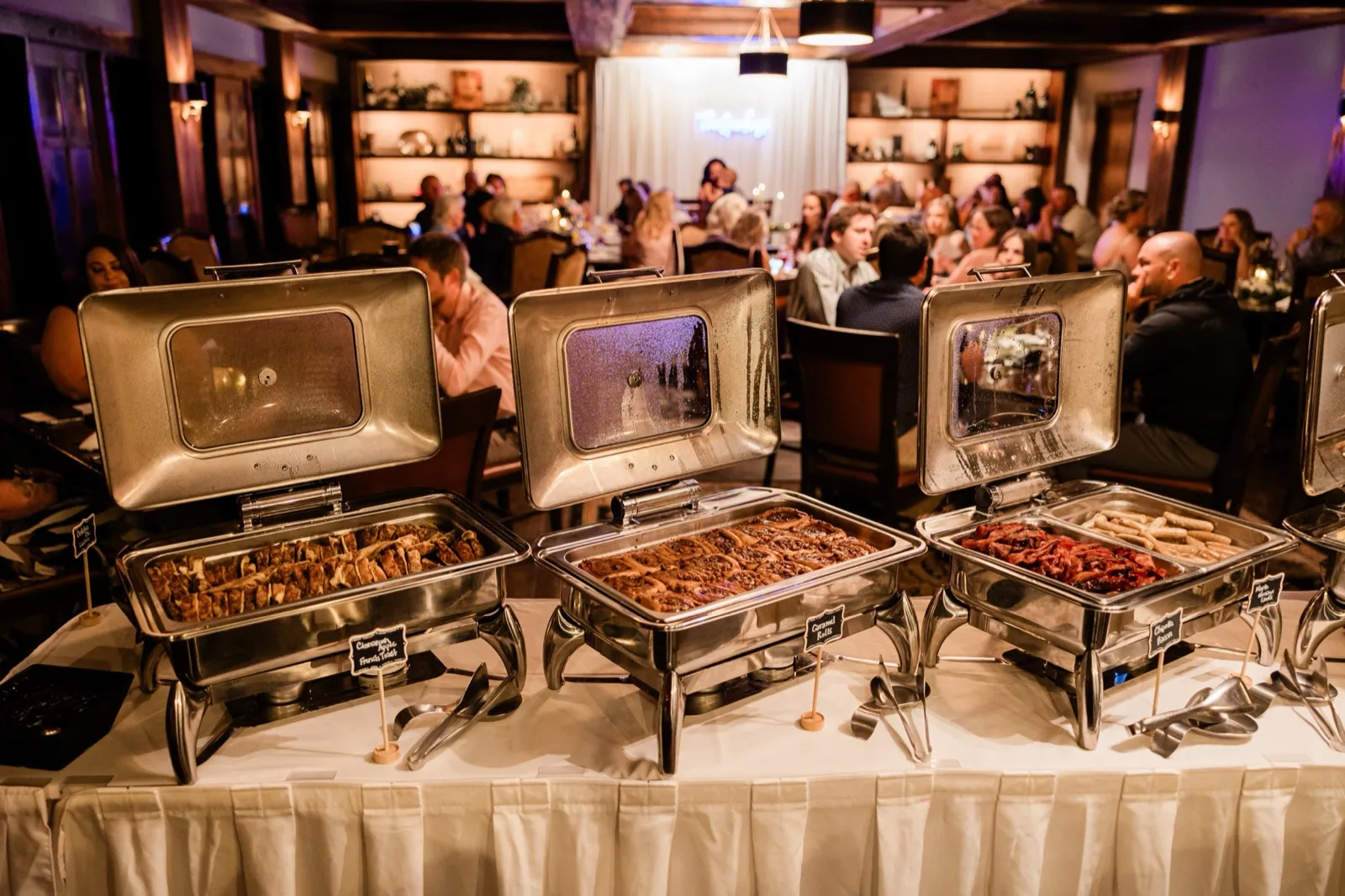 Chafing dishes of french toast, caramel rolls, bacon, and sausage line the brunch buffet as guests dine behind — Tim Larsen Photography, Brainerd Lakes MN