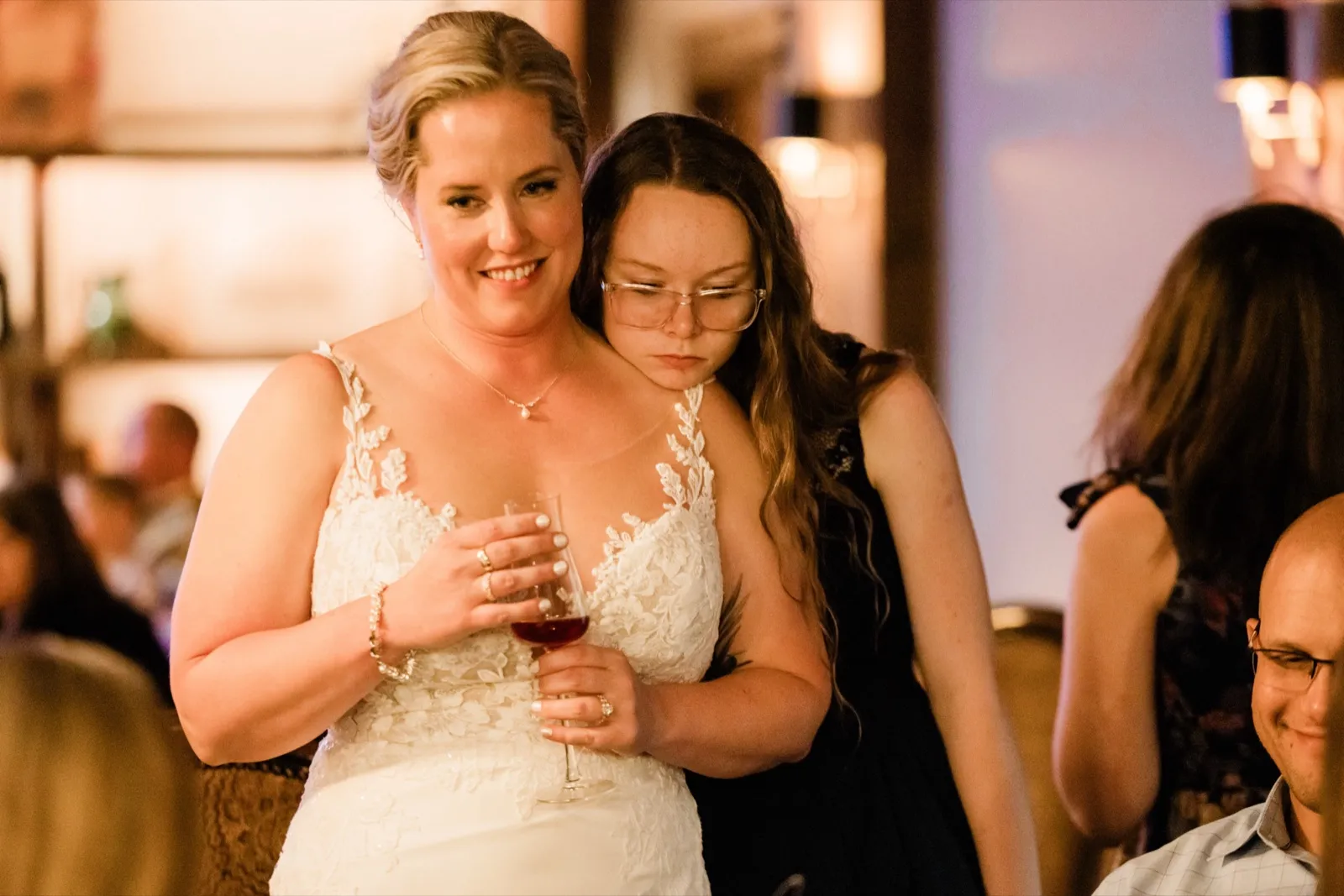 A young guest rests her head on Lauren's shoulder, eyes closed, as the bride smiles softly — Tim Larsen Photography, Brainerd Lakes MN