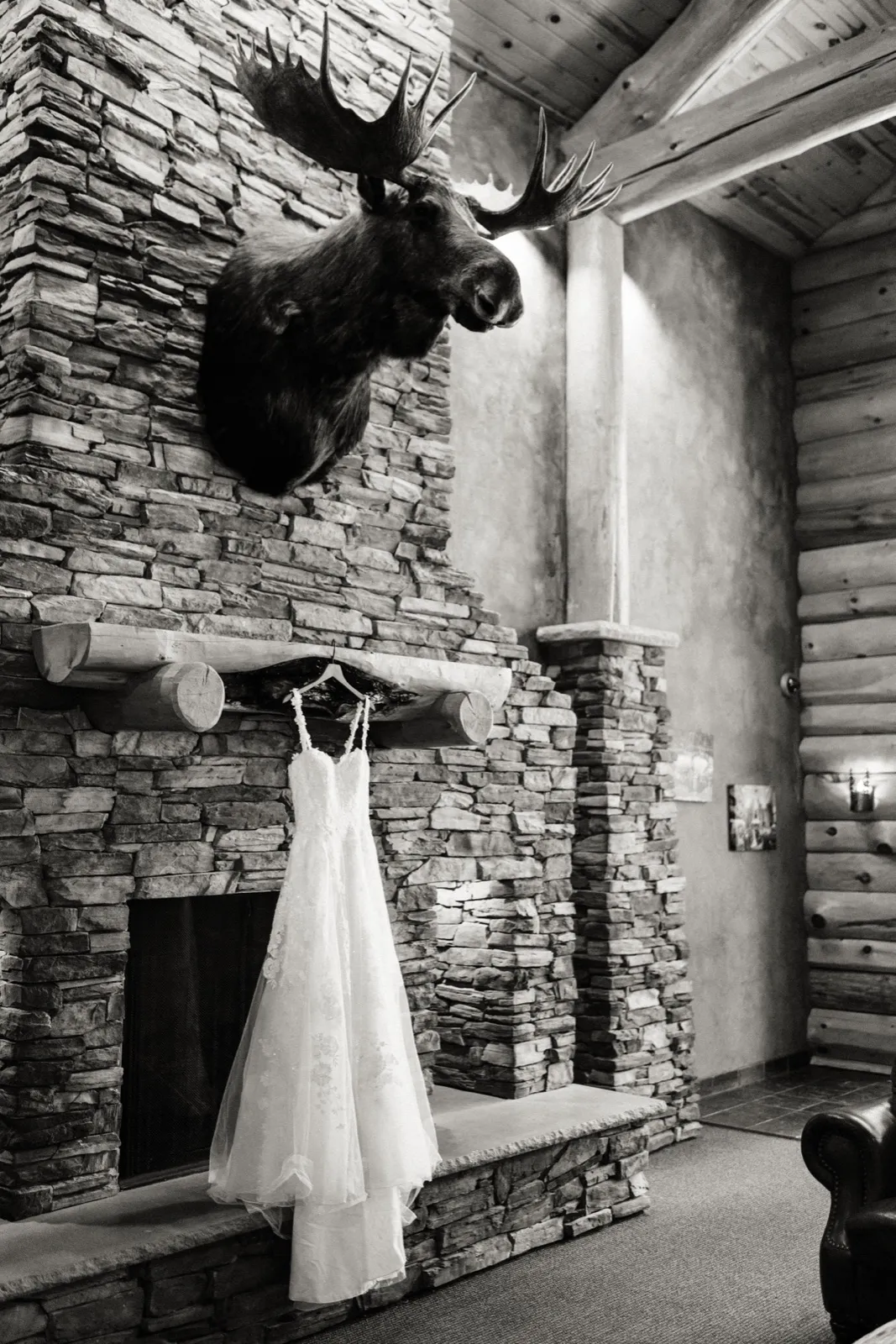 Maddie’s wedding dress hangs against the stone fireplace beneath a mounted moose at Whitefish Lodge — Tim Larsen Photography, Brainerd Lakes MN