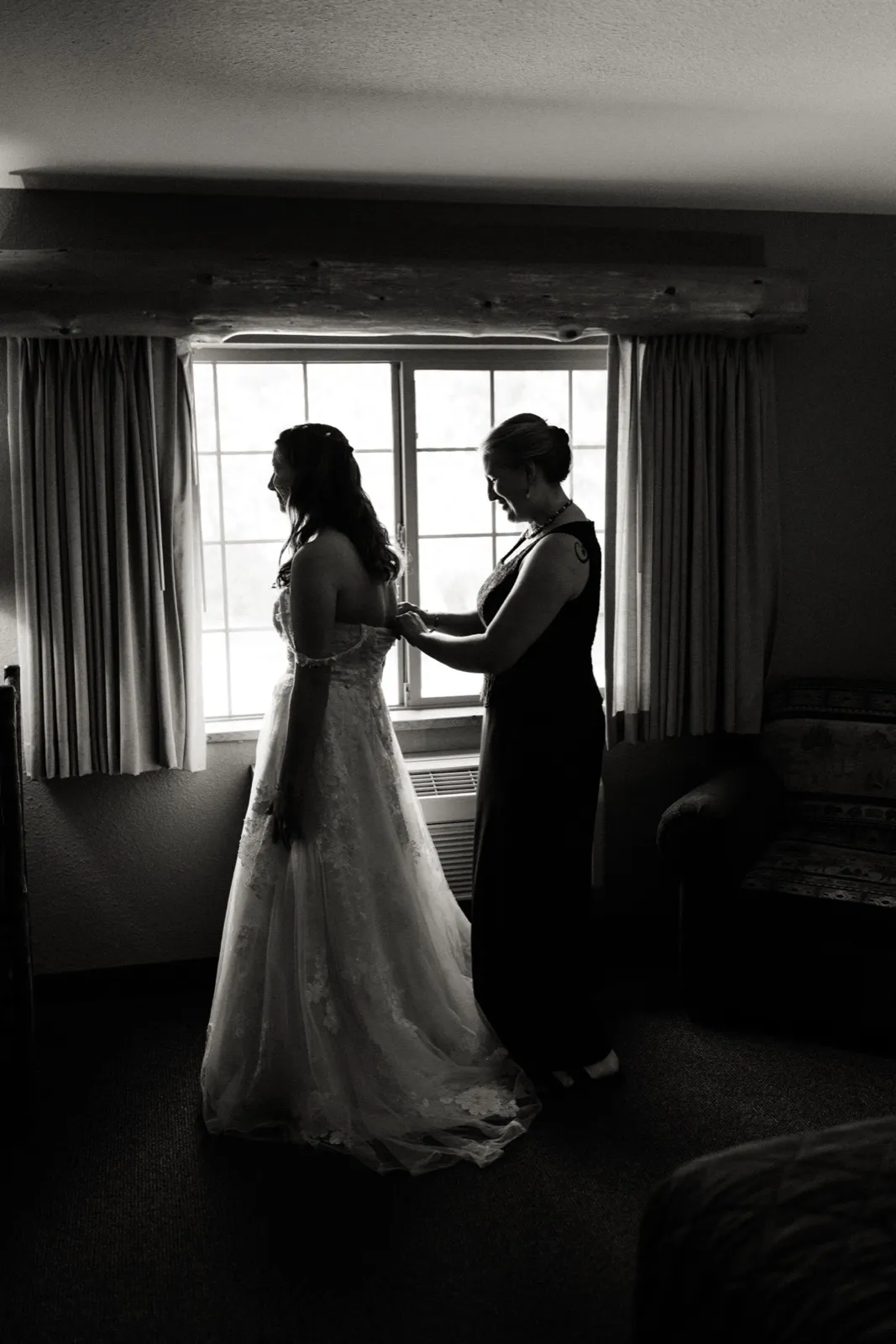 Maddie and a woman helping with her gown are silhouetted against a bright window — Tim Larsen Photography, Brainerd Lakes MN