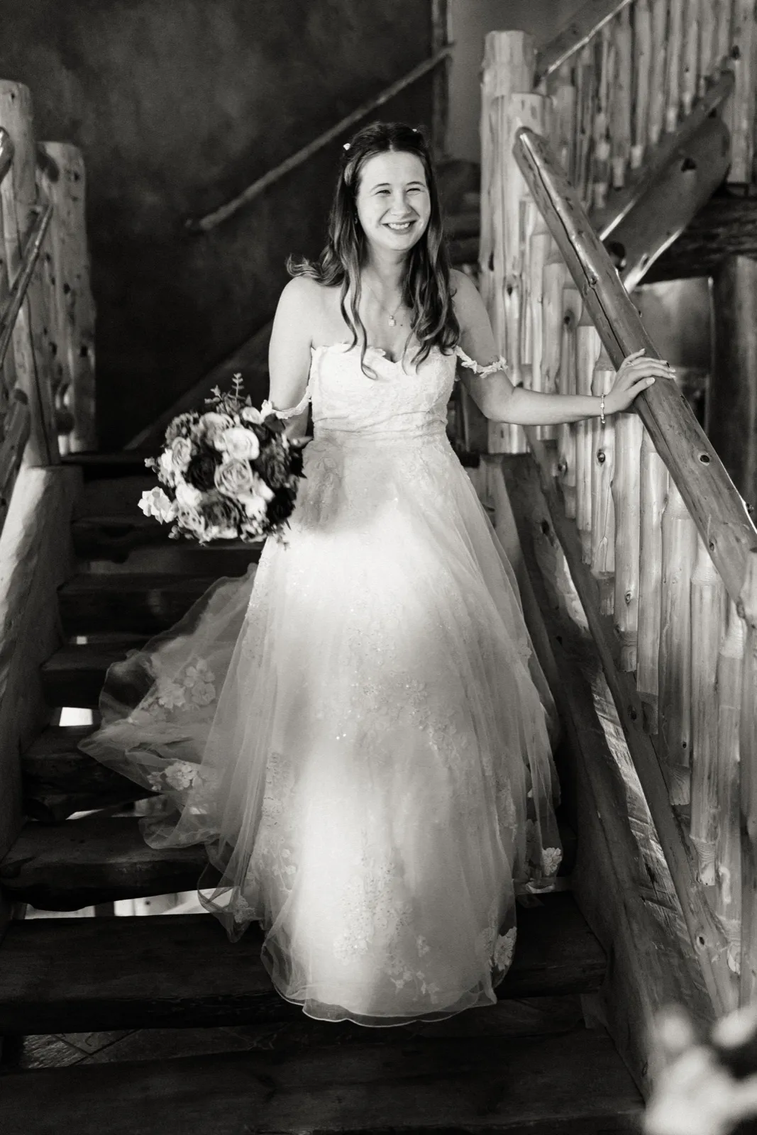 Maddie smiles as she comes down the log staircase with her bouquet at Whitefish Lodge — Tim Larsen Photography, Brainerd Lakes MN