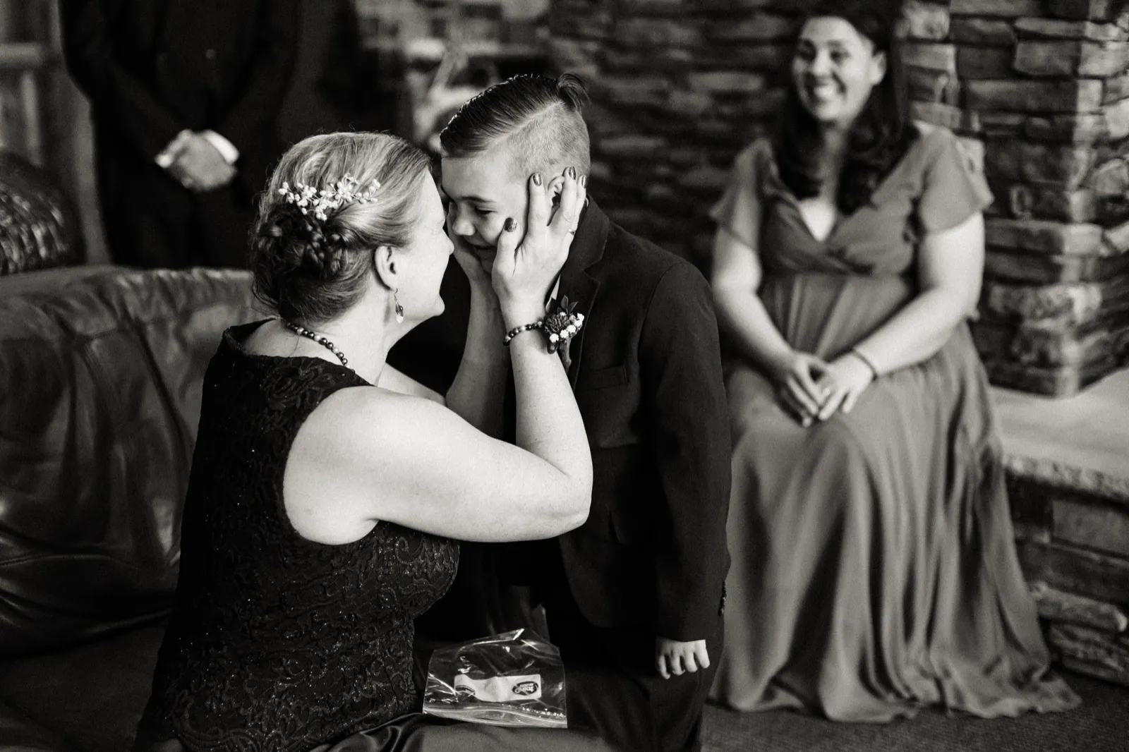 A woman cups Cody’s cheek beside the stone fireplace in a black-and-white photograph — Tim Larsen Photography, Brainerd Lakes MN