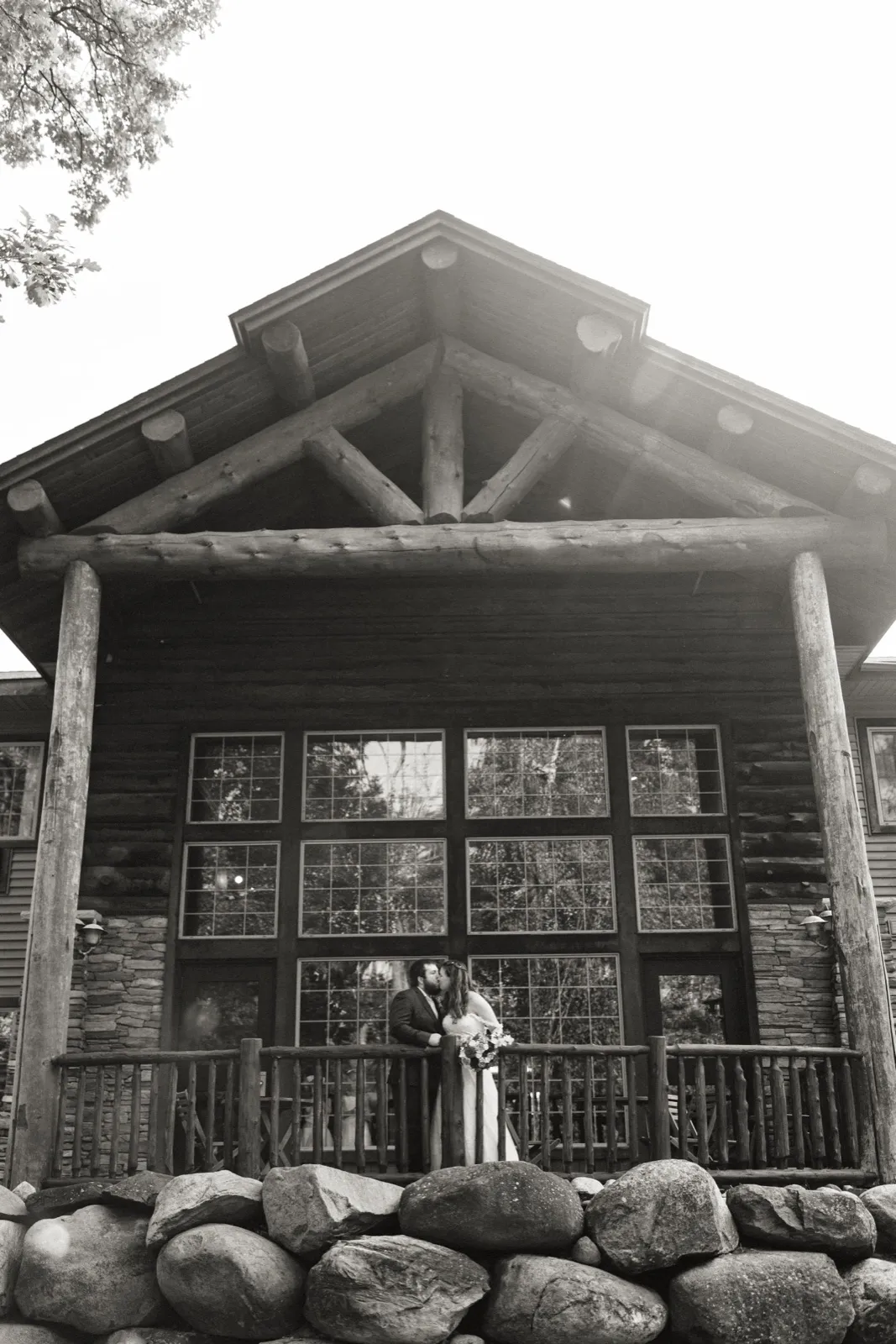 Maddie and Cody kiss on the timber porch at Whitefish Lodge in a black-and-white portrait — Tim Larsen Photography, Brainerd Lakes MN