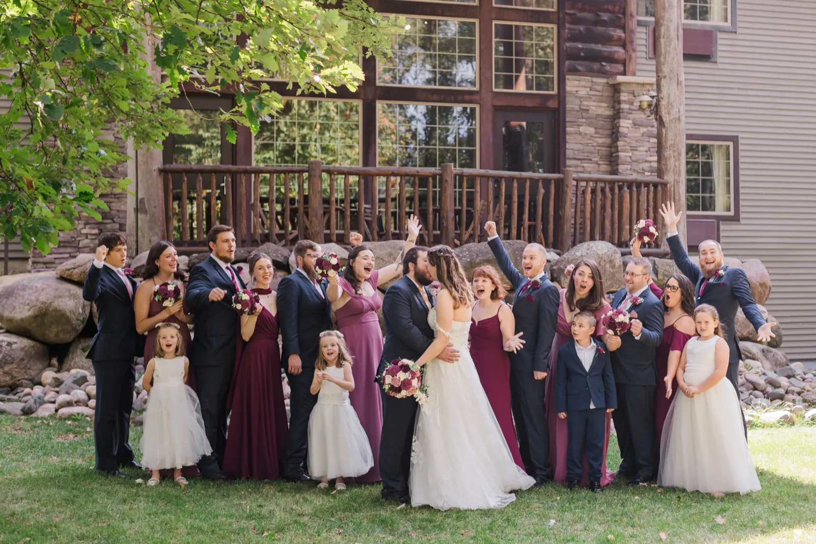 The wedding party cheers as Maddie and Cody kiss on the lawn beside Whitefish Lodge — Tim Larsen Photography, Brainerd Lakes MN
