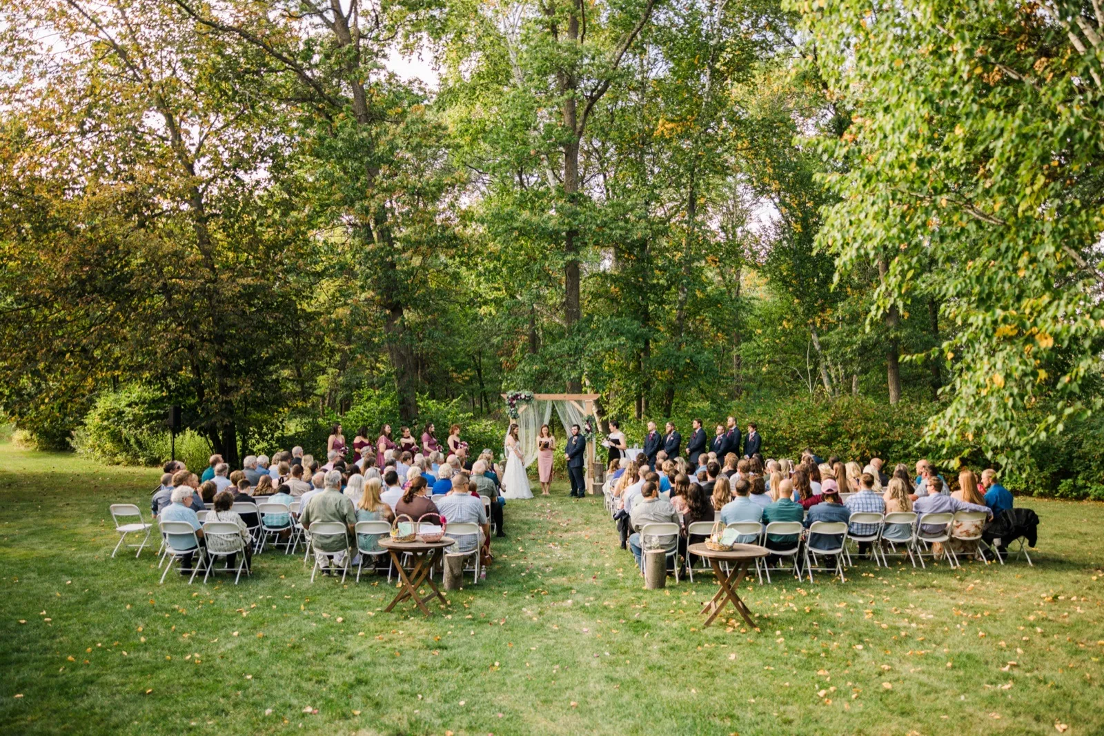 Guests sit in rows on the lawn facing Maddie and Cody’s ceremony arch beneath leafy trees — Tim Larsen Photography, Brainerd Lakes MN