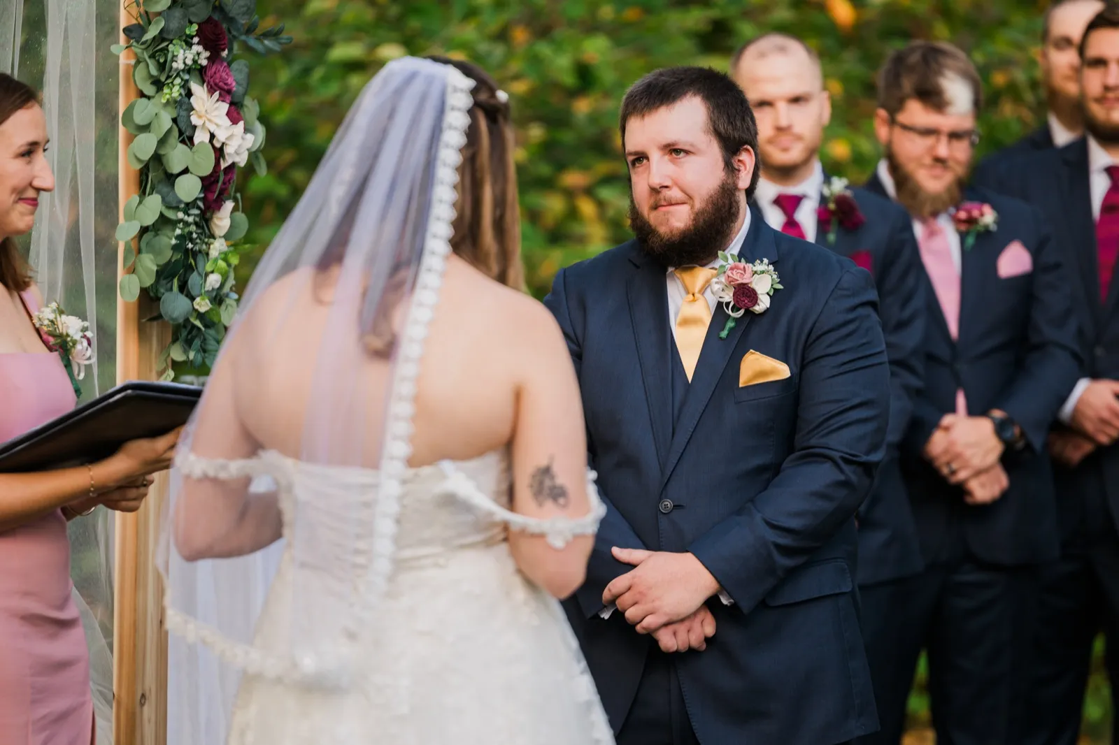 Cody looks toward Maddie during their vows, with groomsmen behind him — Tim Larsen Photography, Brainerd Lakes MN