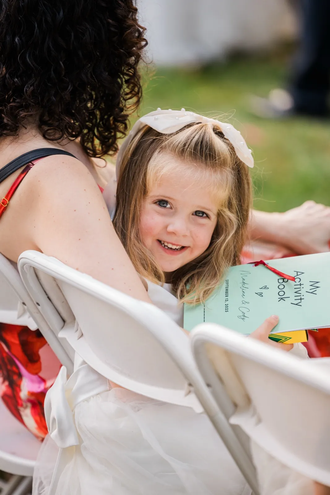 A young girl looks back over a folding chair while holding an activity book during the ceremony — Tim Larsen Photography, Brainerd Lakes MN