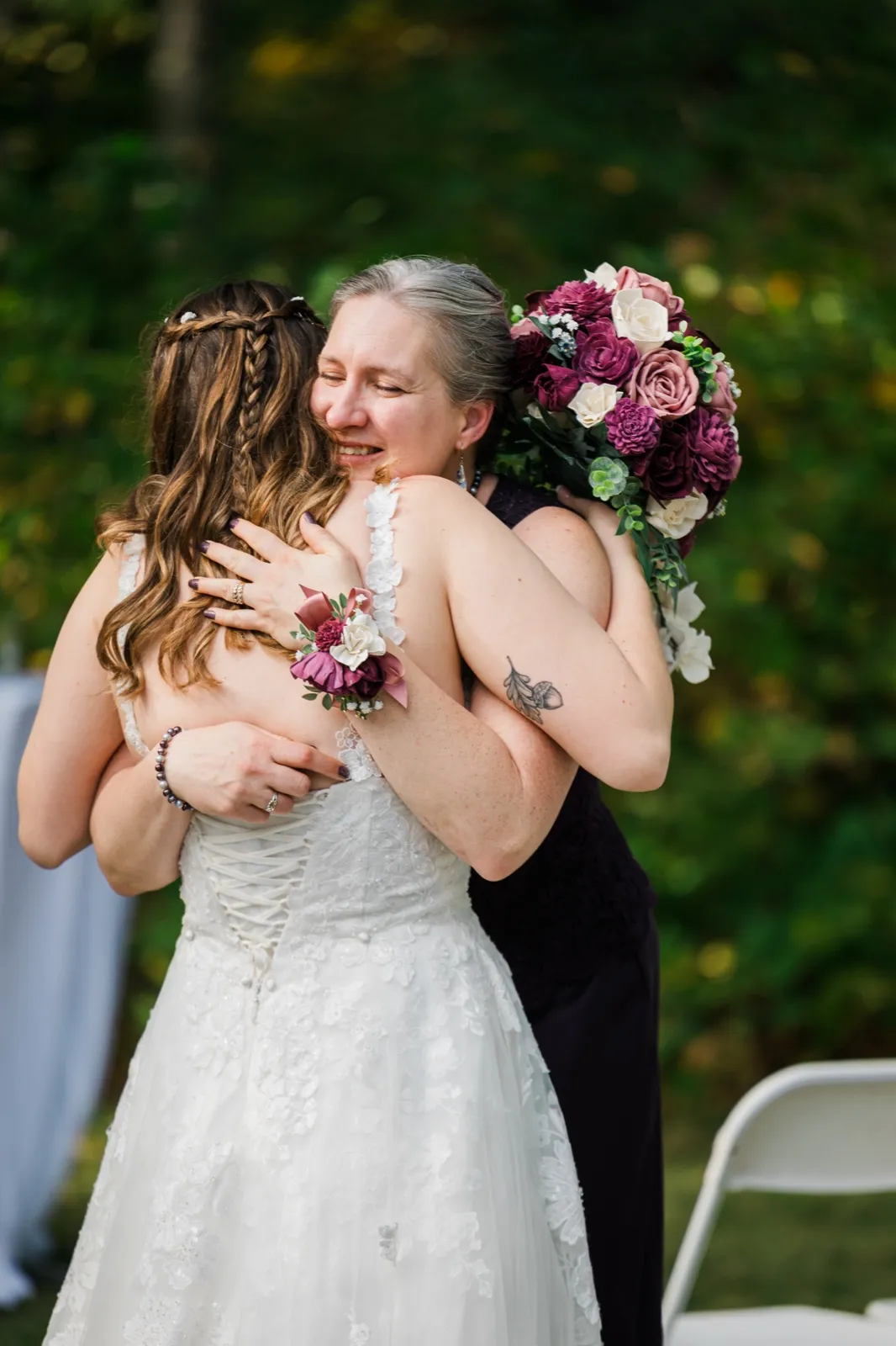 Maddie embraces a woman holding a burgundy and blush bouquet after the ceremony — Tim Larsen Photography, Brainerd Lakes MN