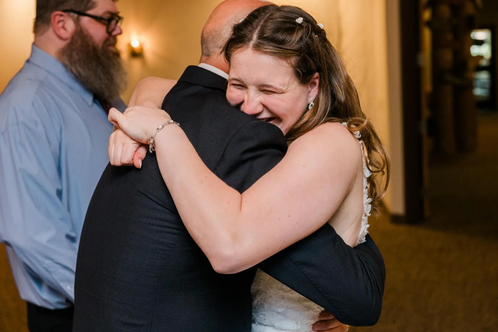 Maddie hugs a man in a dark suit after the ceremony as another guest smiles beside them — Tim Larsen Photography, Brainerd Lakes MN