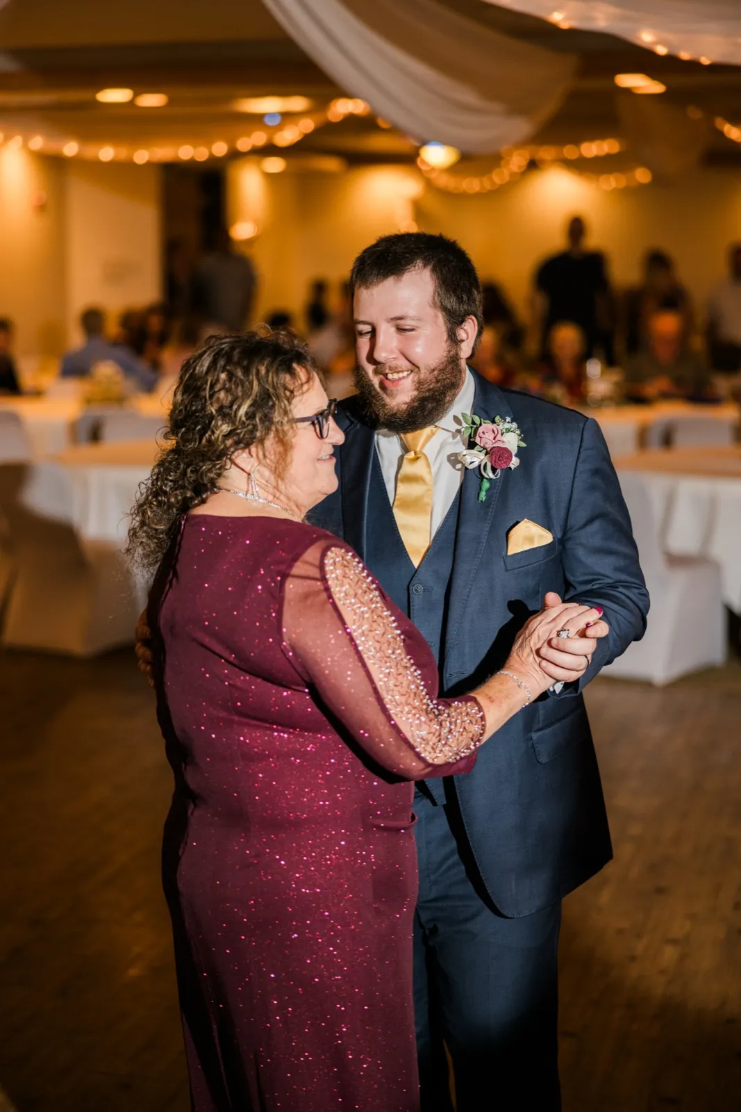 Cody dances with a woman in a burgundy dress beneath string lights at Whitefish Lodge — Tim Larsen Photography, Brainerd Lakes MN