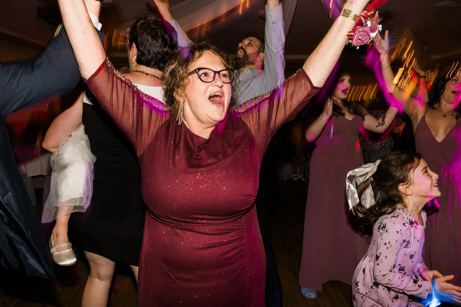 A guest in a burgundy dress throws both arms up on the dance floor at Whitefish Lodge — Tim Larsen Photography, Brainerd Lakes MN