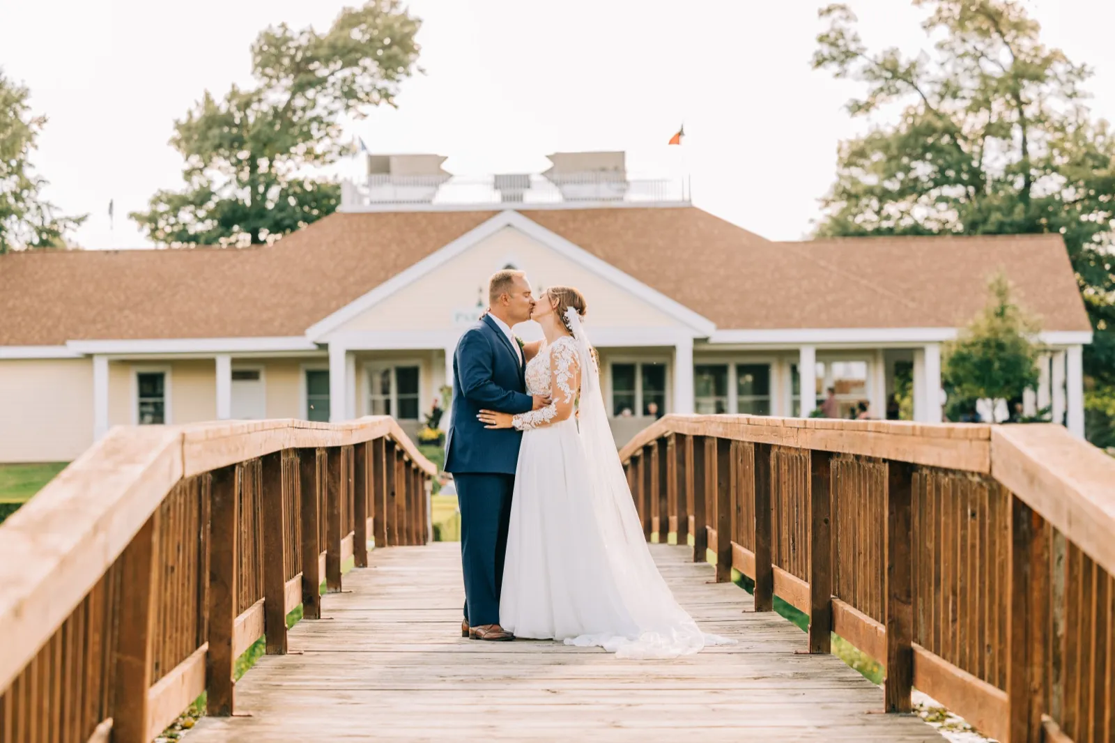 The bride and groom kiss at the center of a wooden bridge with the Madden's Pavilion building visible in the background. — Tim Larsen Photography, Brainerd Lakes MN
