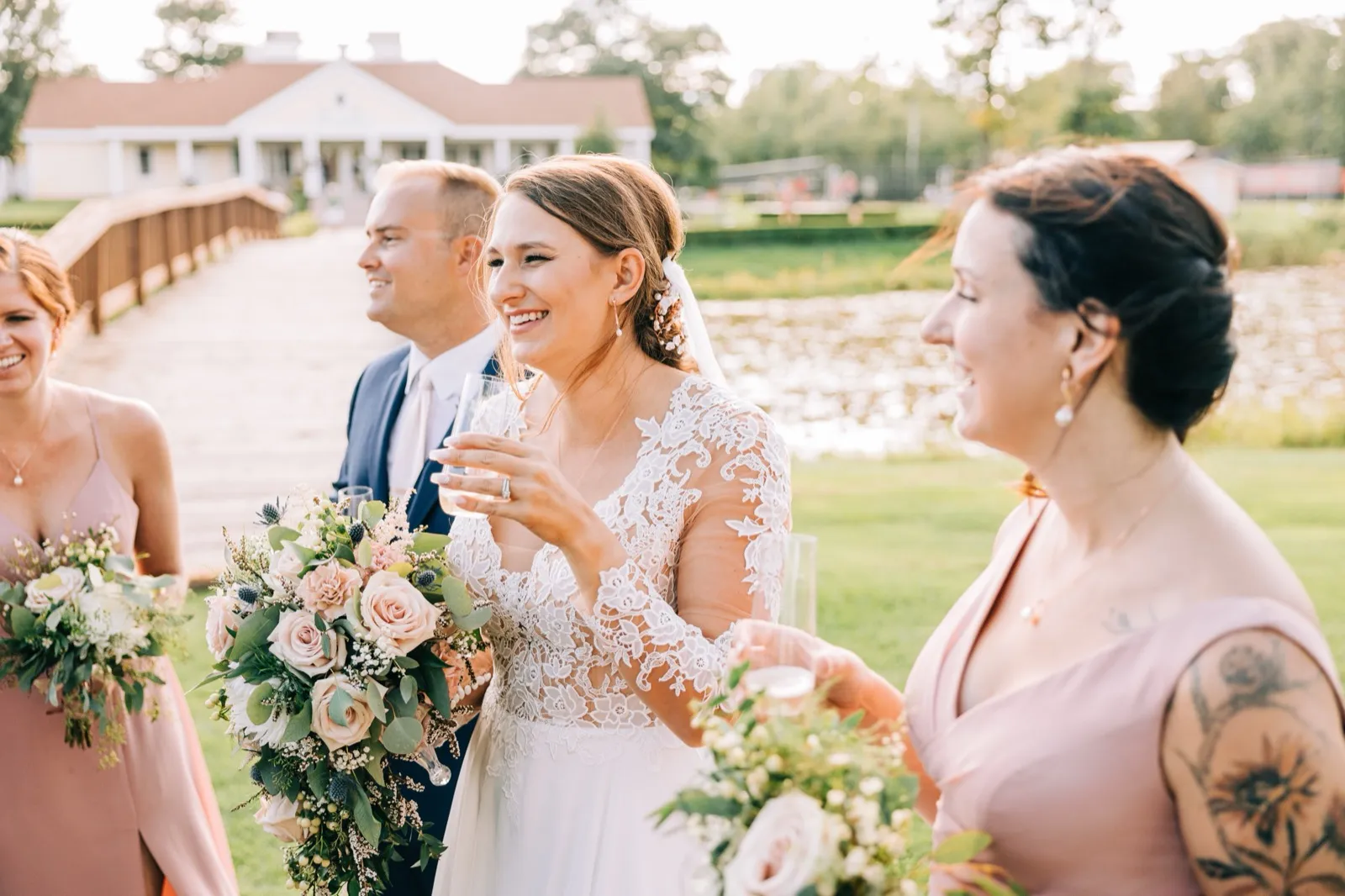 The bride laughs while holding a champagne glass and bouquet, flanked by the groom and bridesmaids on a wooden bridge with the Madden's lodge and Gull Lake behind them. — Tim Larsen Photography, Brainerd Lakes MN
