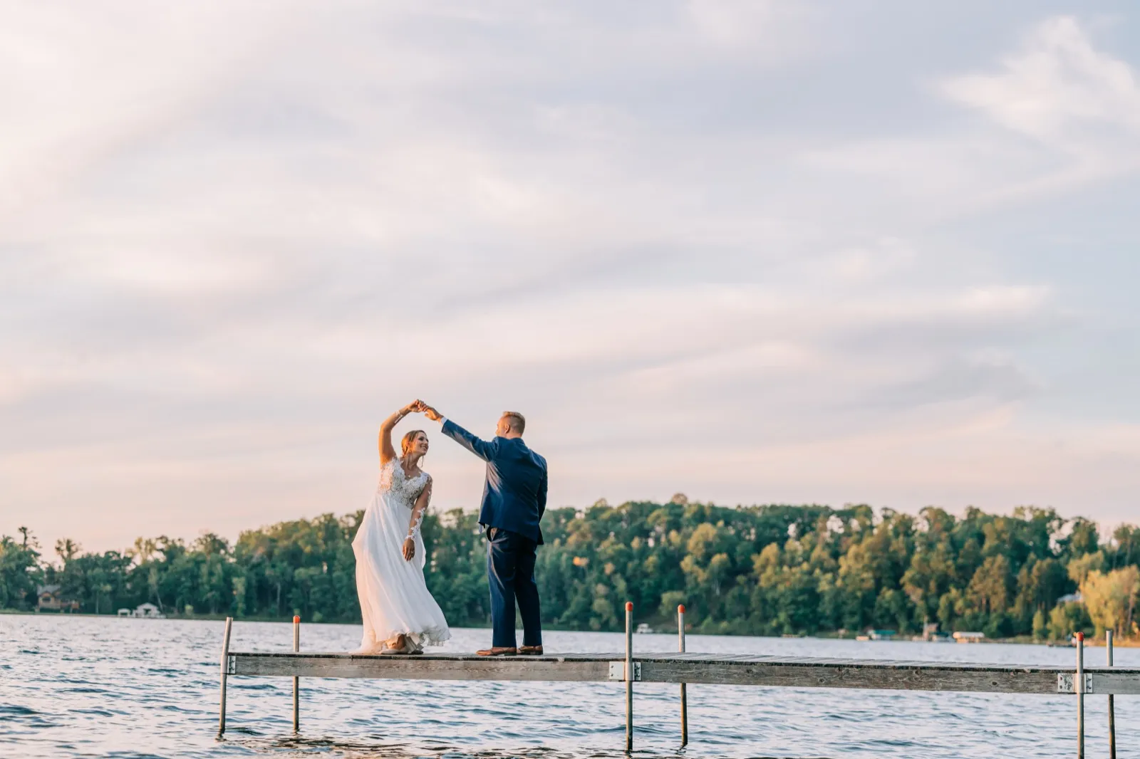 The groom twirls the bride on a wooden dock extending into Gull Lake, with a pastel evening sky and tree-lined far shore behind them. — Tim Larsen Photography, Brainerd Lakes MN