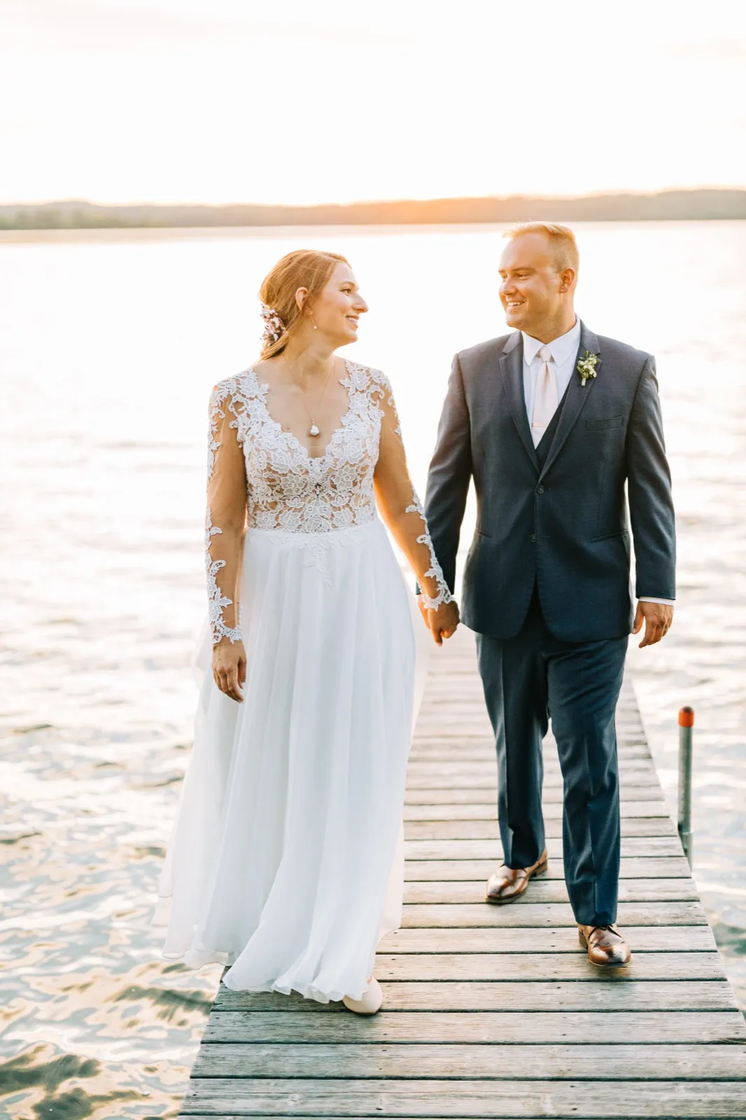 The bride and groom hold hands and look at each other while walking down a wooden dock at sunset over Gull Lake. — Tim Larsen Photography, Brainerd Lakes MN