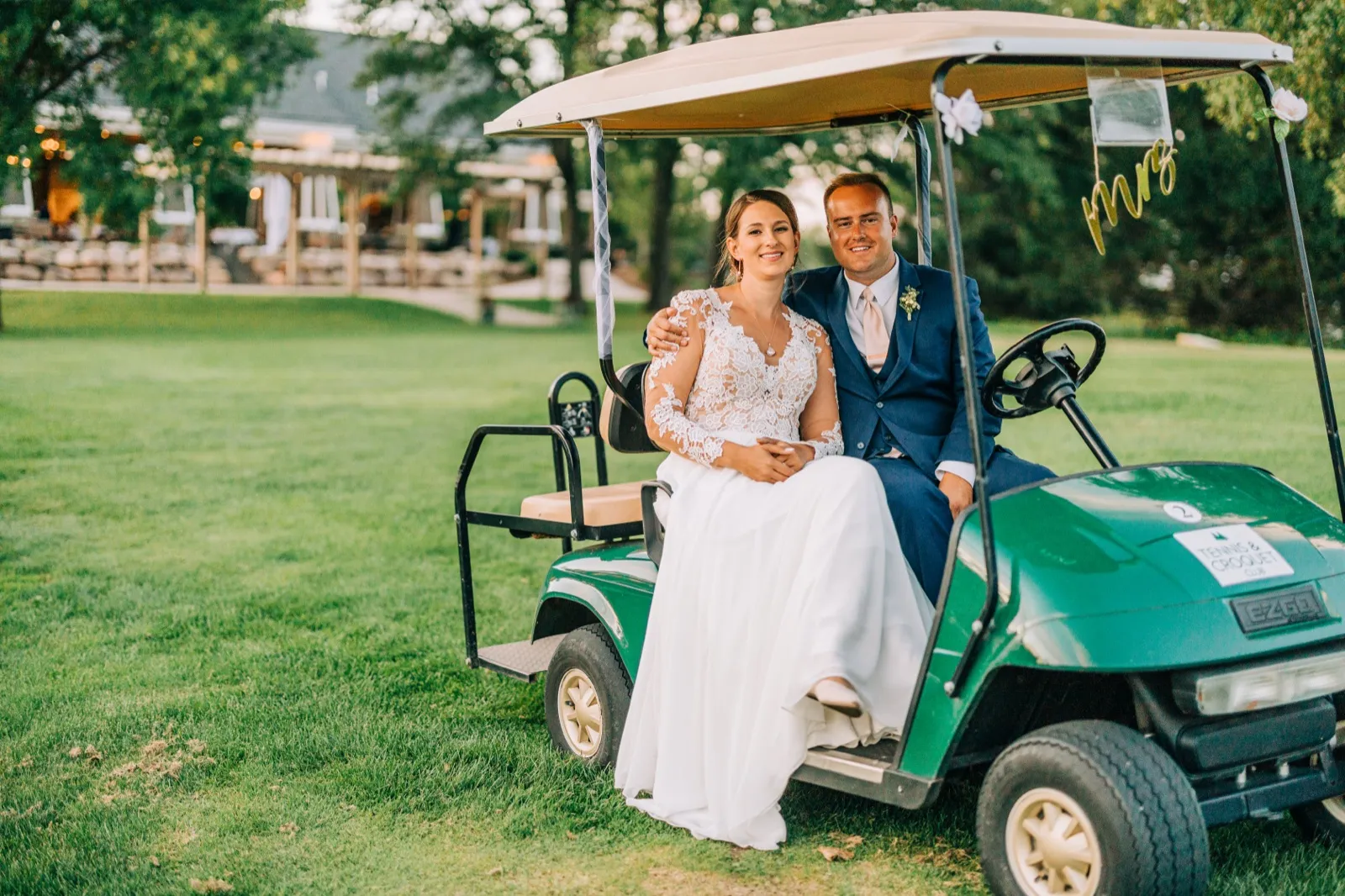 The bride and groom sit together on a green golf cart decorated with a 'Mrs' sign, with the resort lodge visible in the background. — Tim Larsen Photography, Brainerd Lakes MN