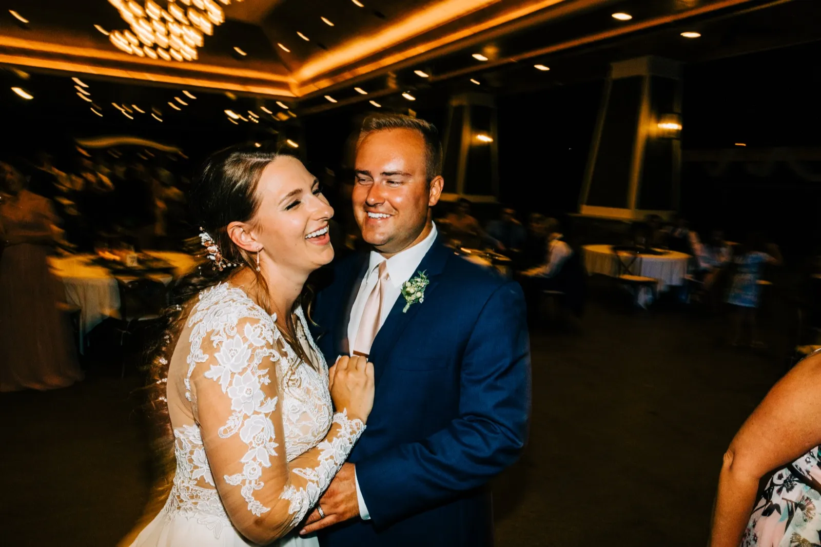 The bride laughs openly while dancing close with the groom on a warmly lit reception floor, her hair and surroundings blurred by motion. — Tim Larsen Photography, Brainerd Lakes MN