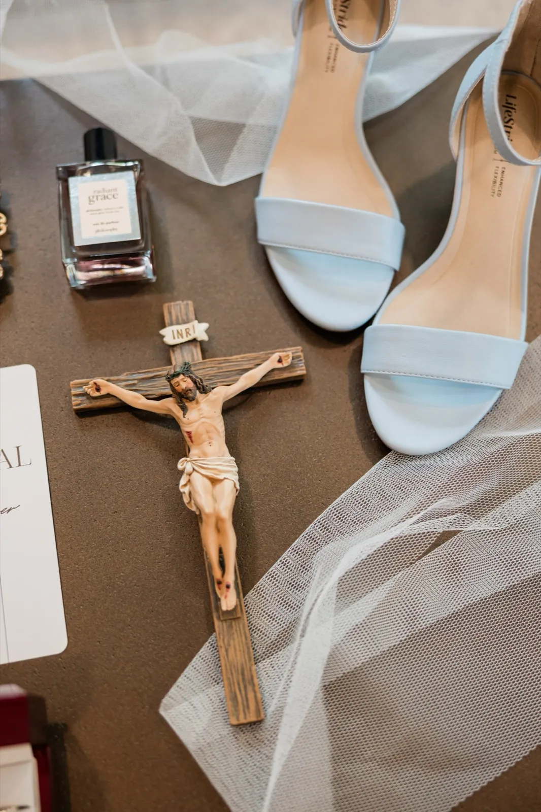 The bride's powder-blue heels, a perfume bottle, and a wooden crucifix rest on a taupe surface with a veil draped alongside — Tim Larsen Photography, Brainerd Lakes MN