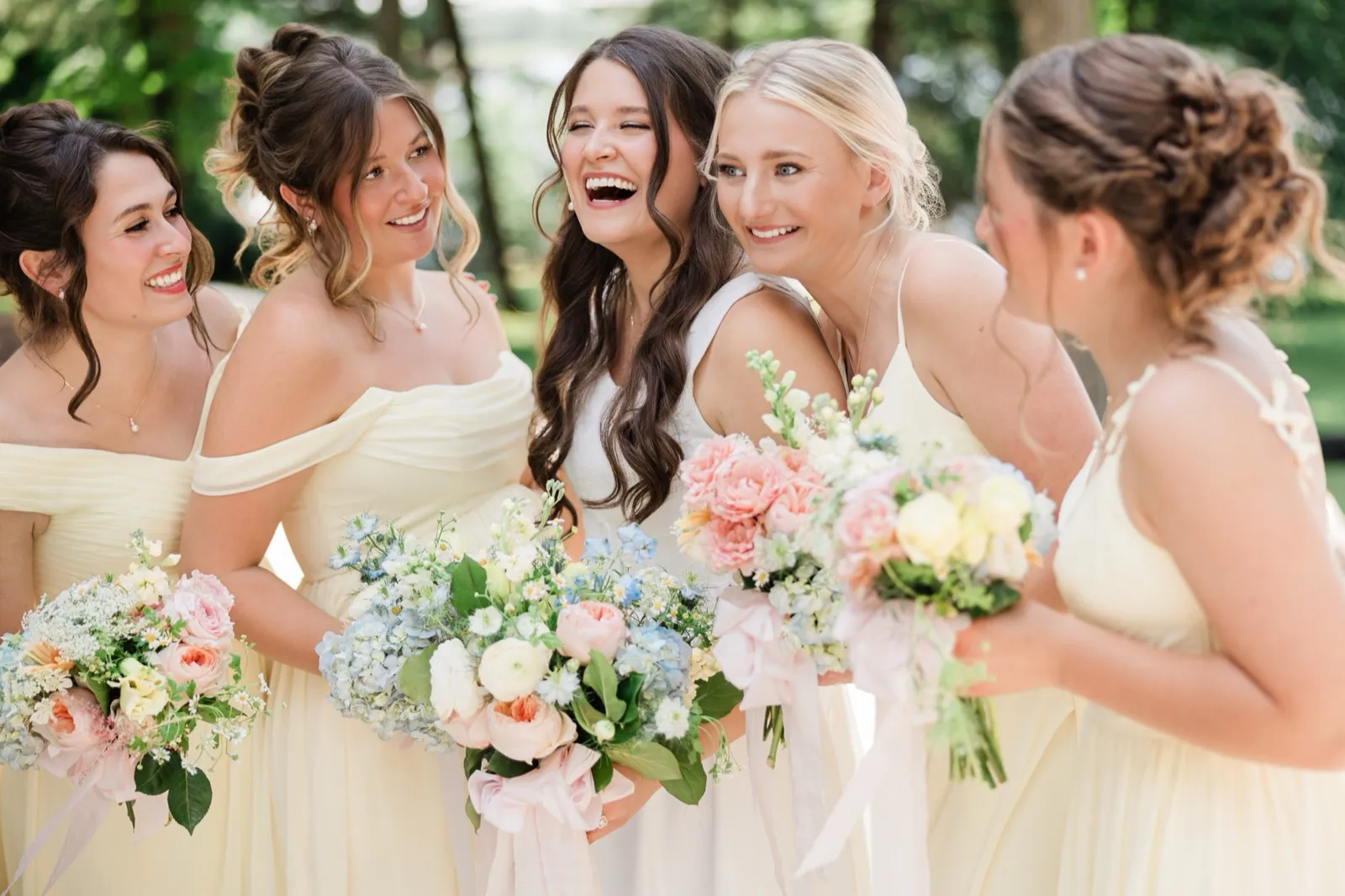 The bride laughs with her eyes closed as her bridesmaids lean in around her, all smiling, outdoors — Tim Larsen Photography, Brainerd Lakes MN