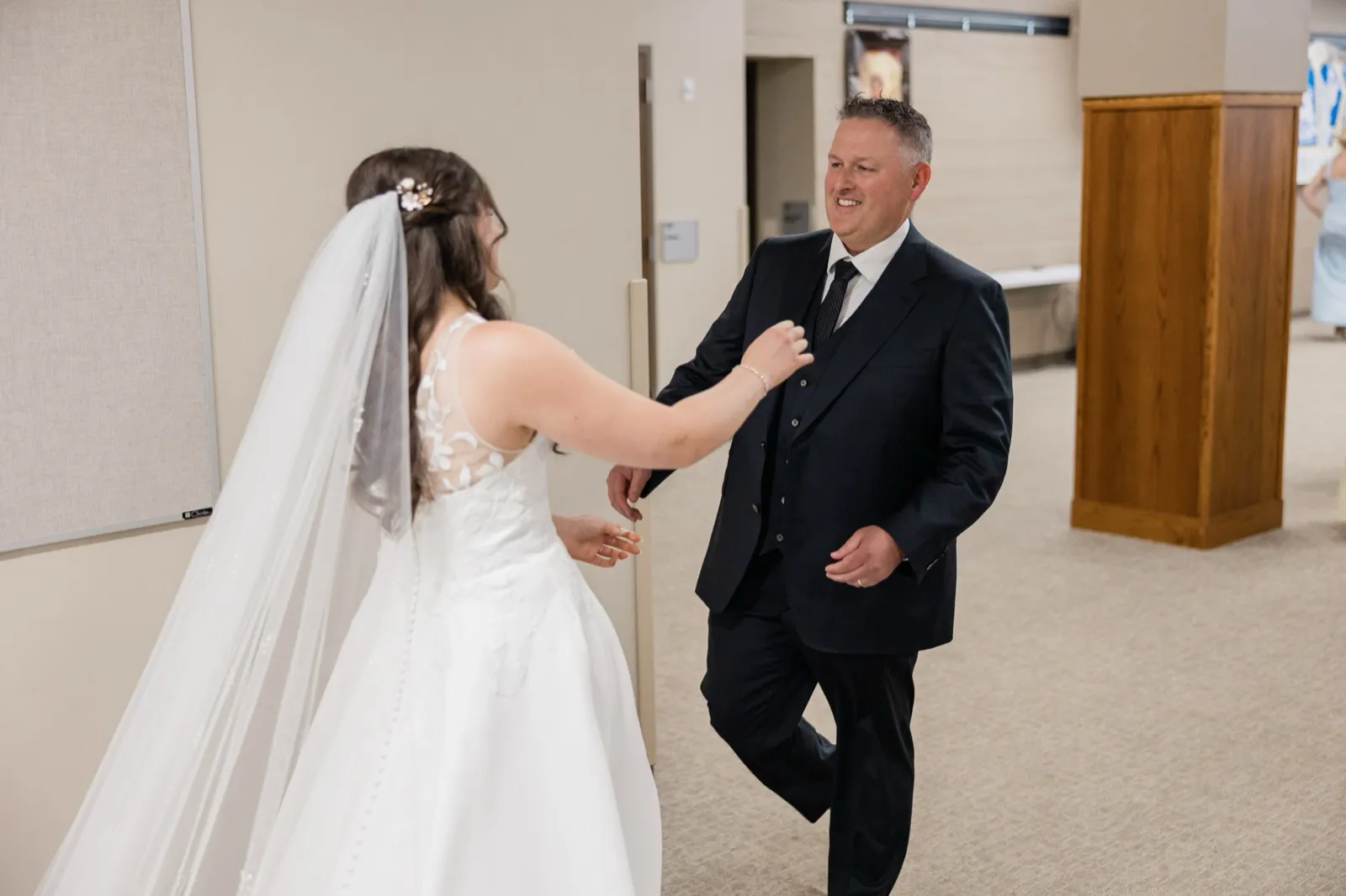 The bride reaches for her father during their first look in a hallway at St. Francis Catholic Church in Brainerd — Tim Larsen Photography, Brainerd Lakes MN