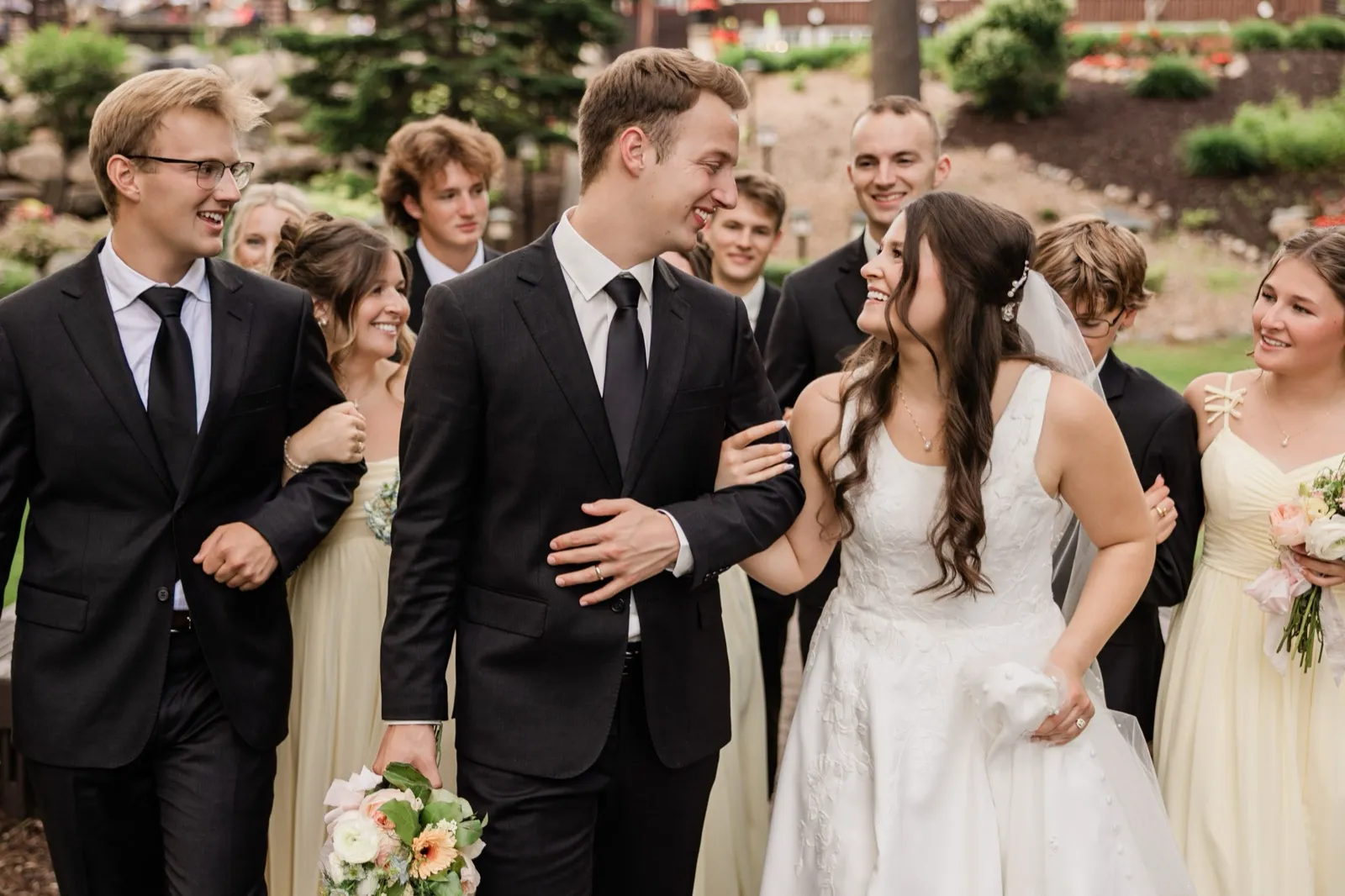The bride and groom laugh together at the center of their wedding party as everyone walks across the lodge grounds — Tim Larsen Photography, Brainerd Lakes MN