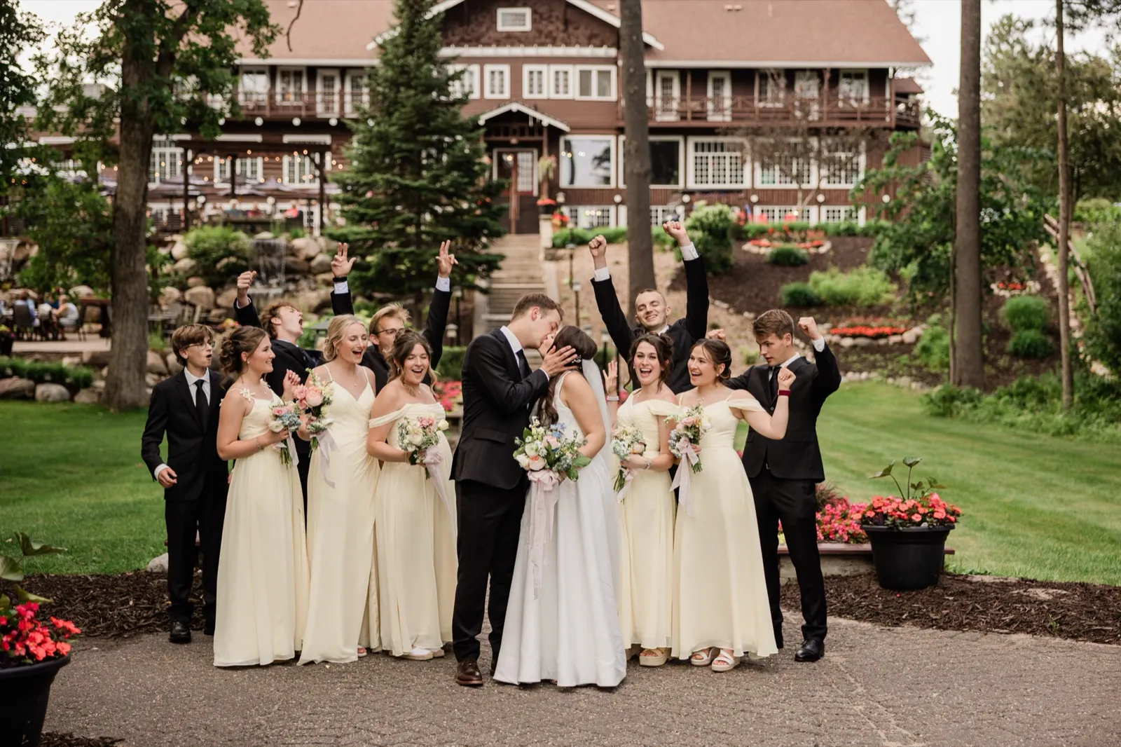 The bride and groom kiss as their wedding party — all brothers and sisters of the couple — cheers around them below the main lodge at Grand View Lodge — Tim Larsen Photography, Brainerd Lakes MN