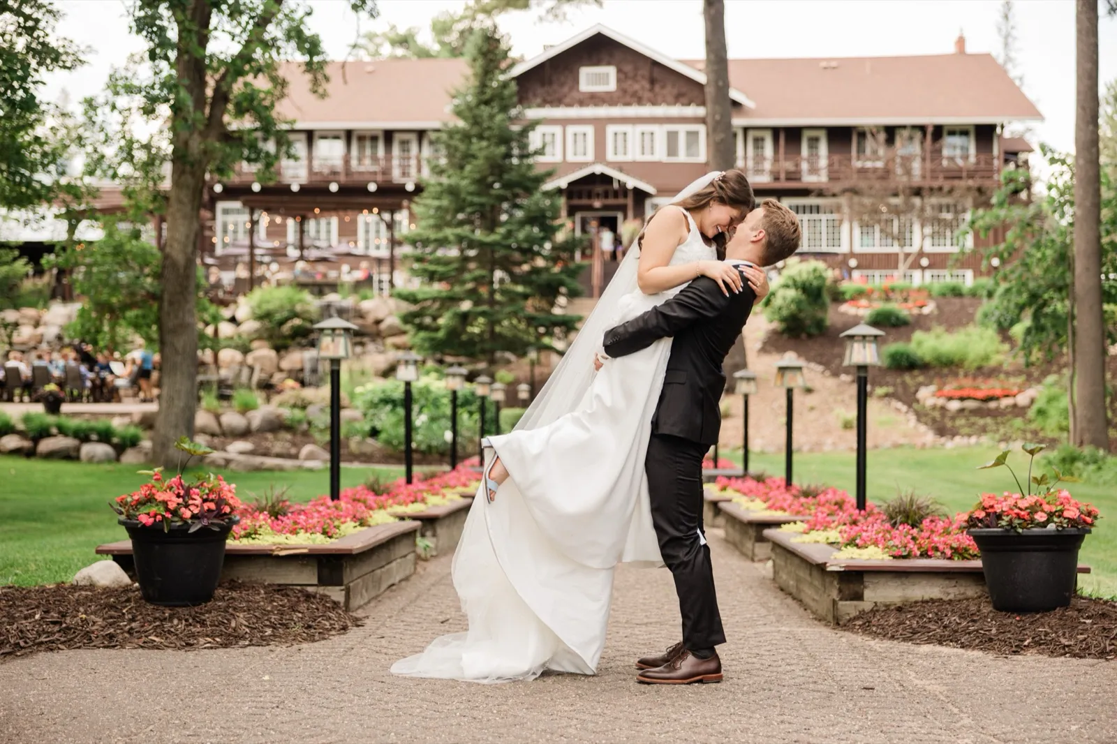 The groom lifts the bride off her feet at the center of the formal garden path at Grand View Lodge in Nisswa, the historic main lodge rising behind them — Tim Larsen Photography, Brainerd Lakes MN