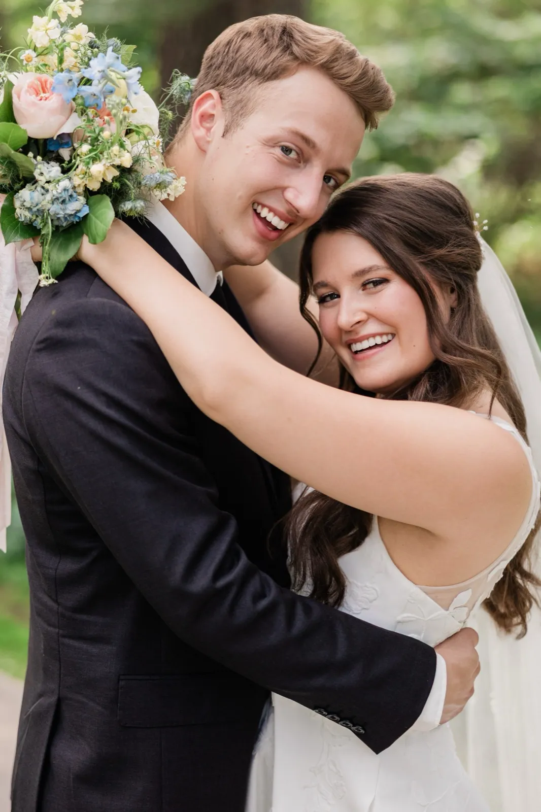 A tight portrait of the bride with her arms wrapped around the groom's neck as both smile broadly at the camera, green trees behind — Tim Larsen Photography, Brainerd Lakes MN