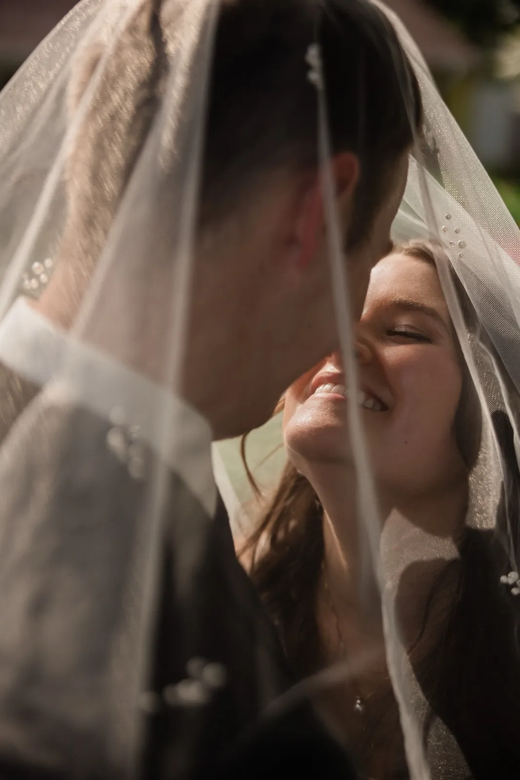 Photographed from beneath the bride's sheer veil, the couple leans nose-to-nose as she laughs with her eyes closed in backlit light — Tim Larsen Photography, Brainerd Lakes MN