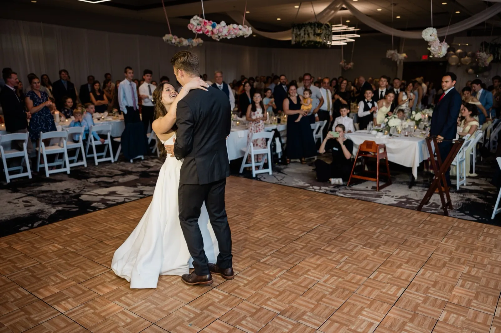 The couple shares their first dance in the center of the floor as guests watch from tables ringing the room — Tim Larsen Photography, Brainerd Lakes MN