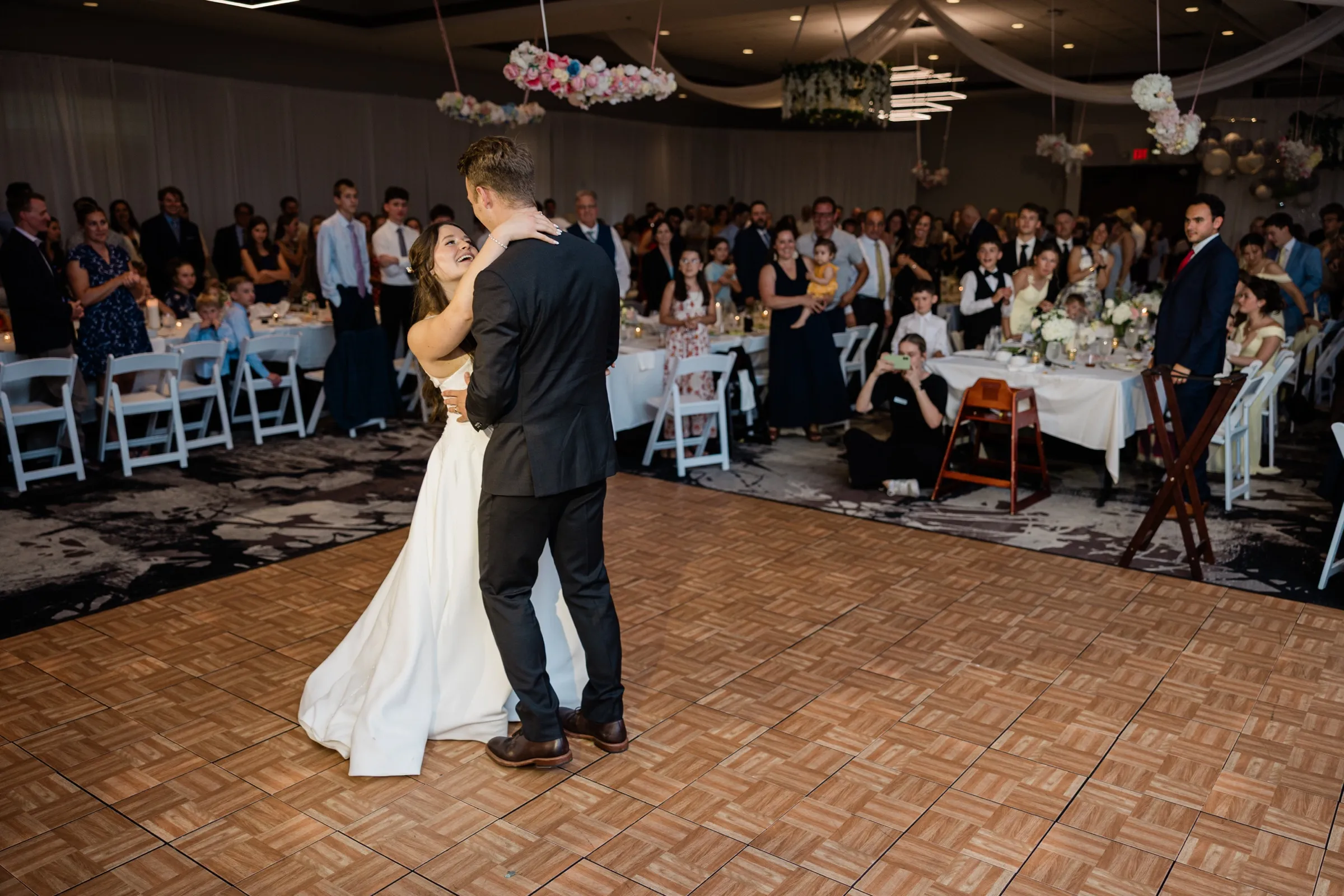 The couple shares their first dance in the center of the floor as guests watch from tables ringing the room — Tim Larsen Photography, Brainerd Lakes MN