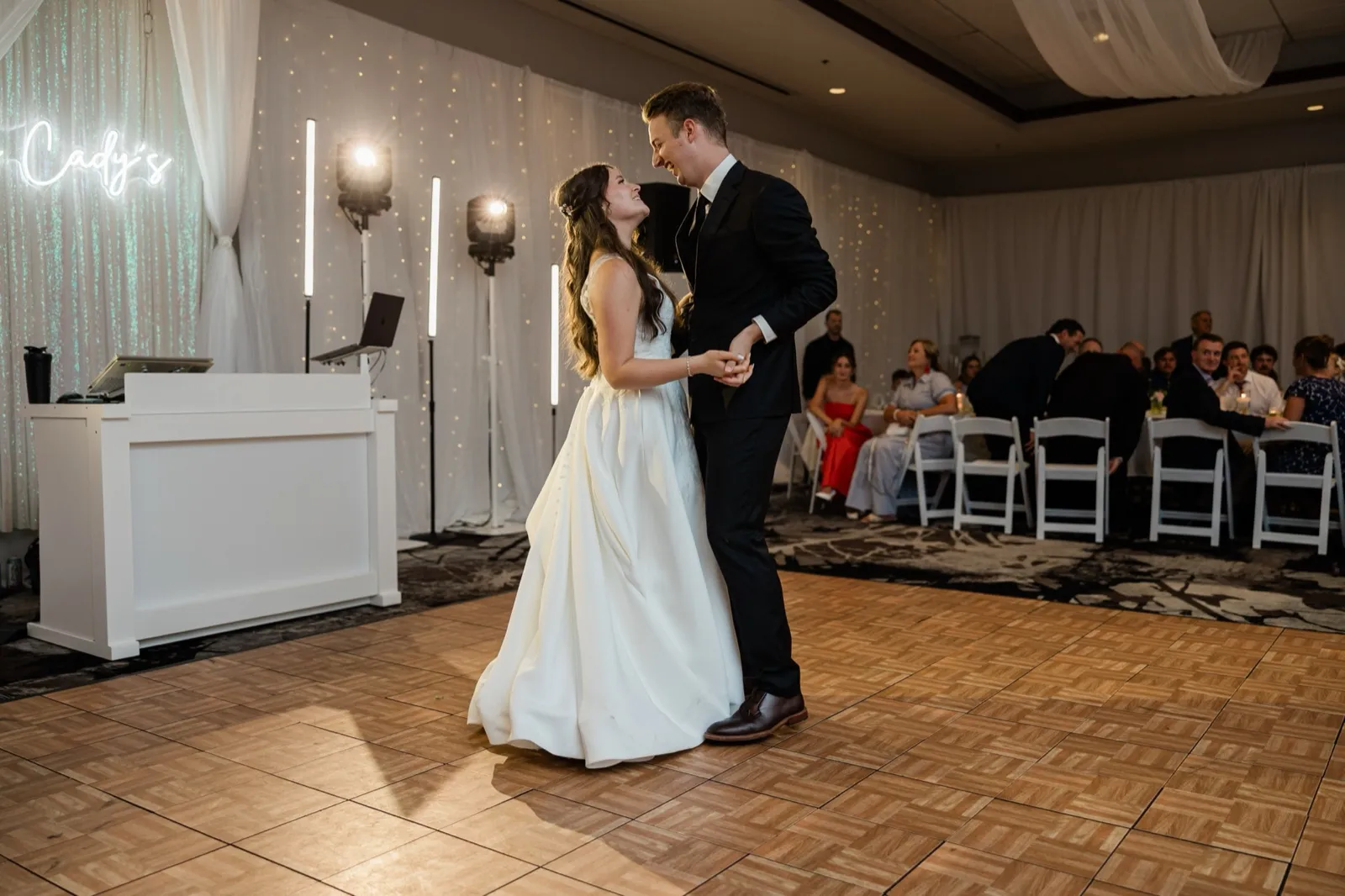 The bride and groom smile into each other's eyes mid-dance in front of a neon sign and fairy-light backdrop — Tim Larsen Photography, Brainerd Lakes MN