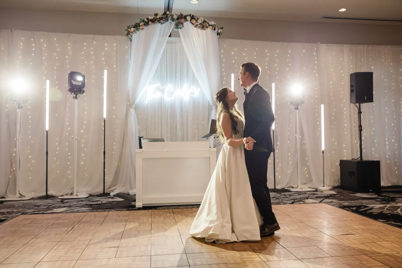 The couple dances centered beneath a floral arch and framed by glowing light towers and a fairy-light backdrop — Tim Larsen Photography, Brainerd Lakes MN