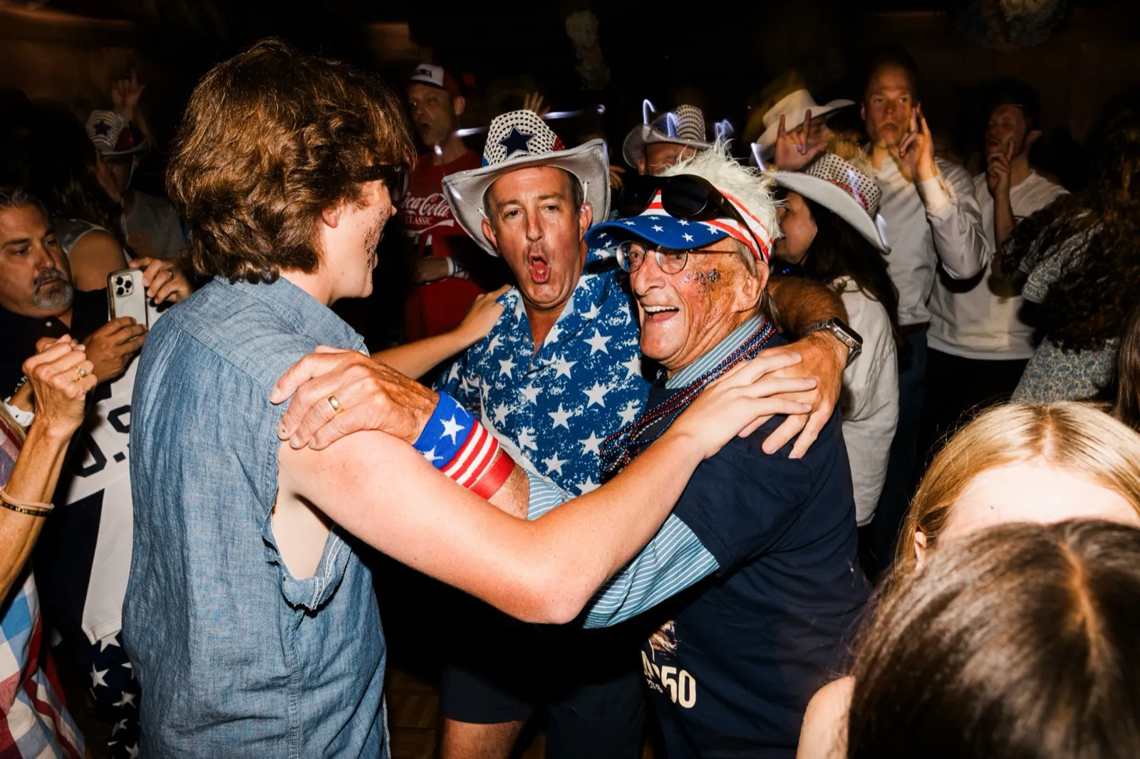 Three men across three generations pull into a laughing group embrace on the dance floor, surrounded by guests in cowboy hats — Tim Larsen Photography, Brainerd Lakes MN