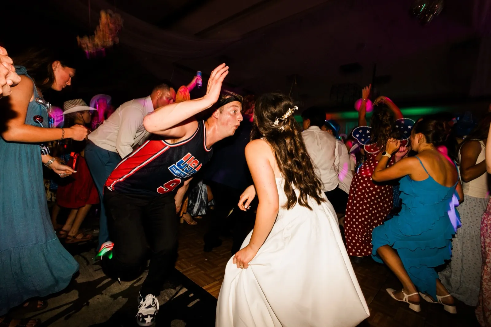 The bride in her white gown dances in the middle of the floor as a guest in a Team USA jersey drops low beside her — Tim Larsen Photography, Brainerd Lakes MN