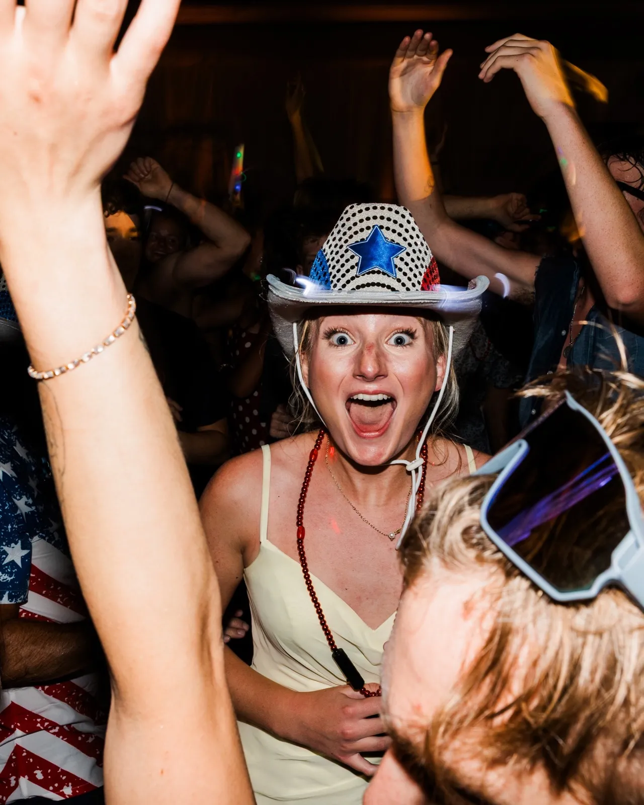 A guest in a star-spangled cowboy hat shouts with delight amid raised arms on the Grand View Lodge dance floor