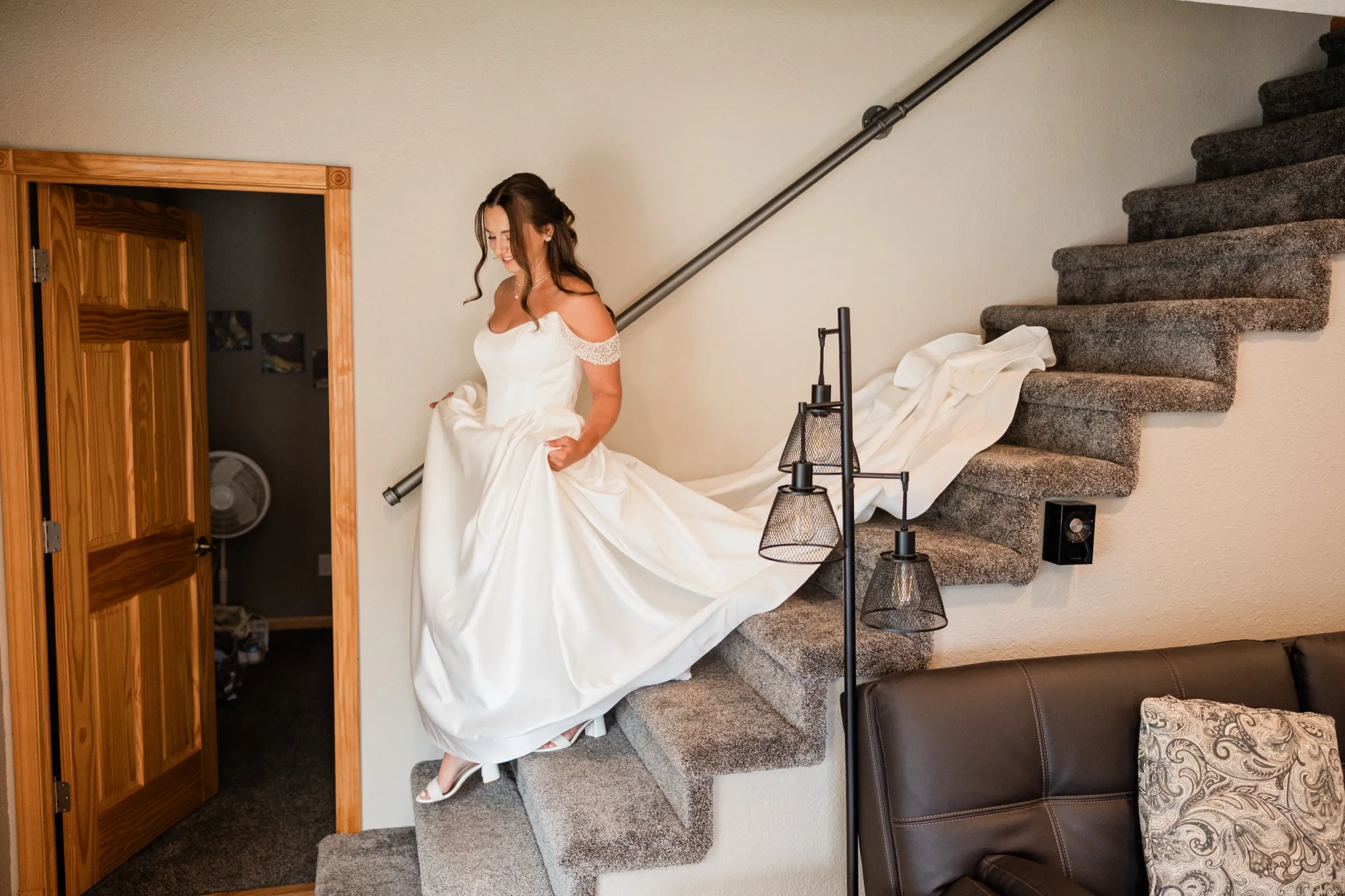 The bride carries her gathered skirt down a carpeted staircase, the train still trailing on the steps above her — Tim Larsen Photography, Brainerd Lakes MN