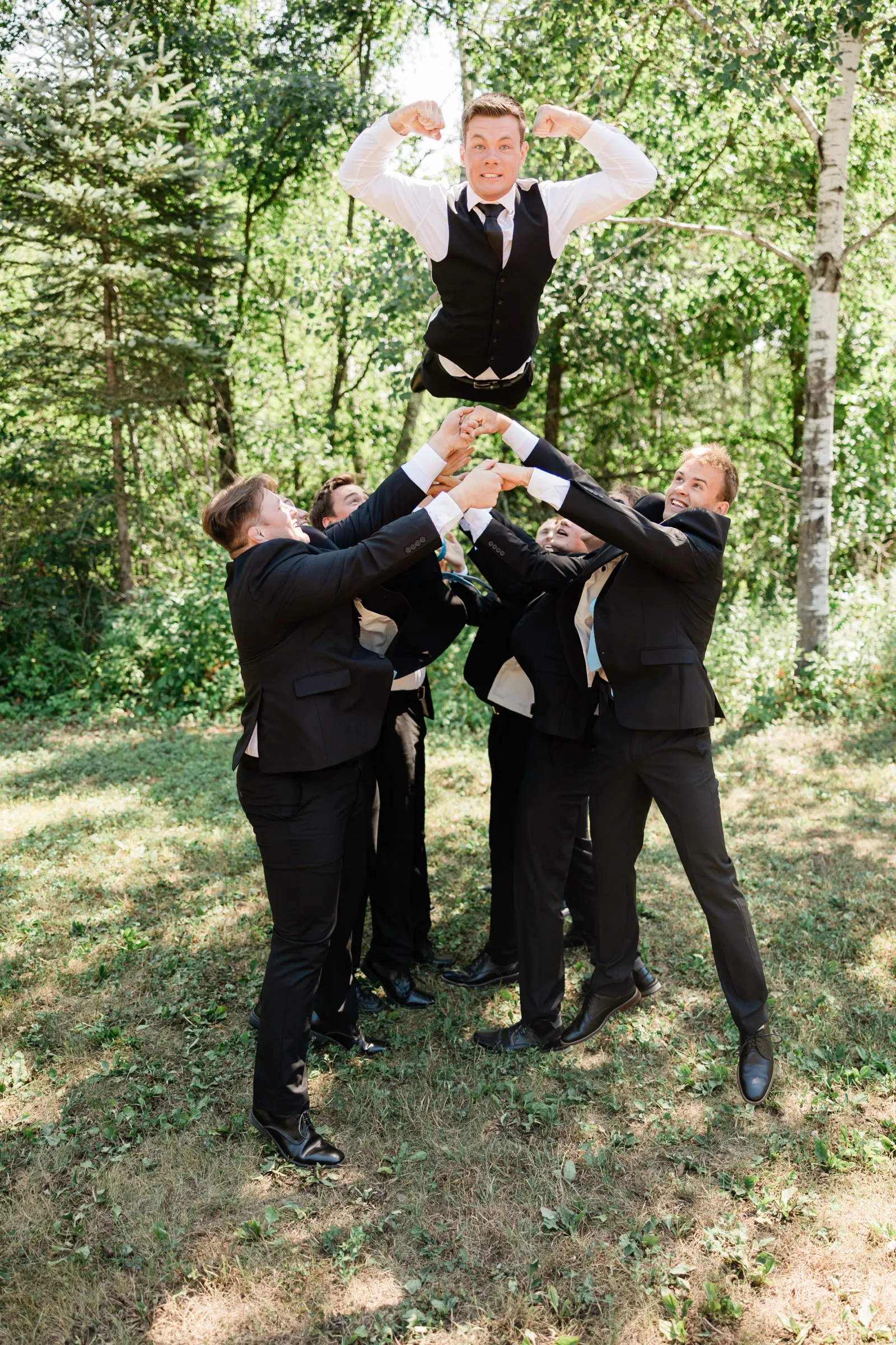 A group of groomsmen hoist another groomsman overhead as he flexes both arms above them — Tim Larsen Photography, Brainerd Lakes MN