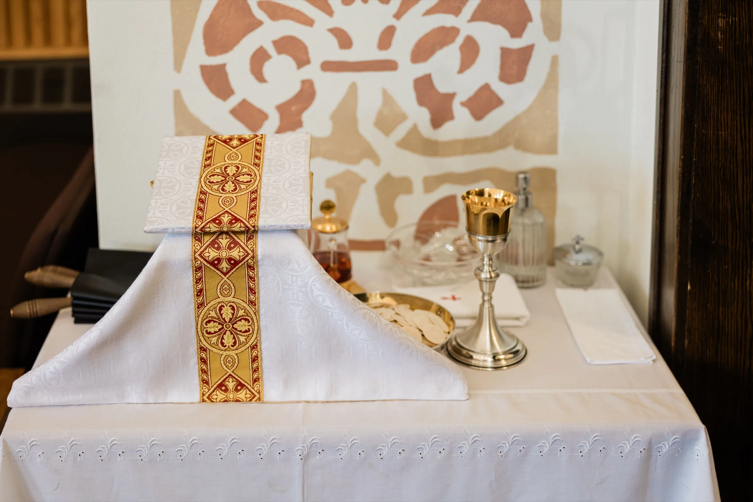 A gold chalice, a paten of hosts and glass cruets sit on a linen-draped table beside a gold and red chalice veil — Tim Larsen Photography, Brainerd Lakes MN