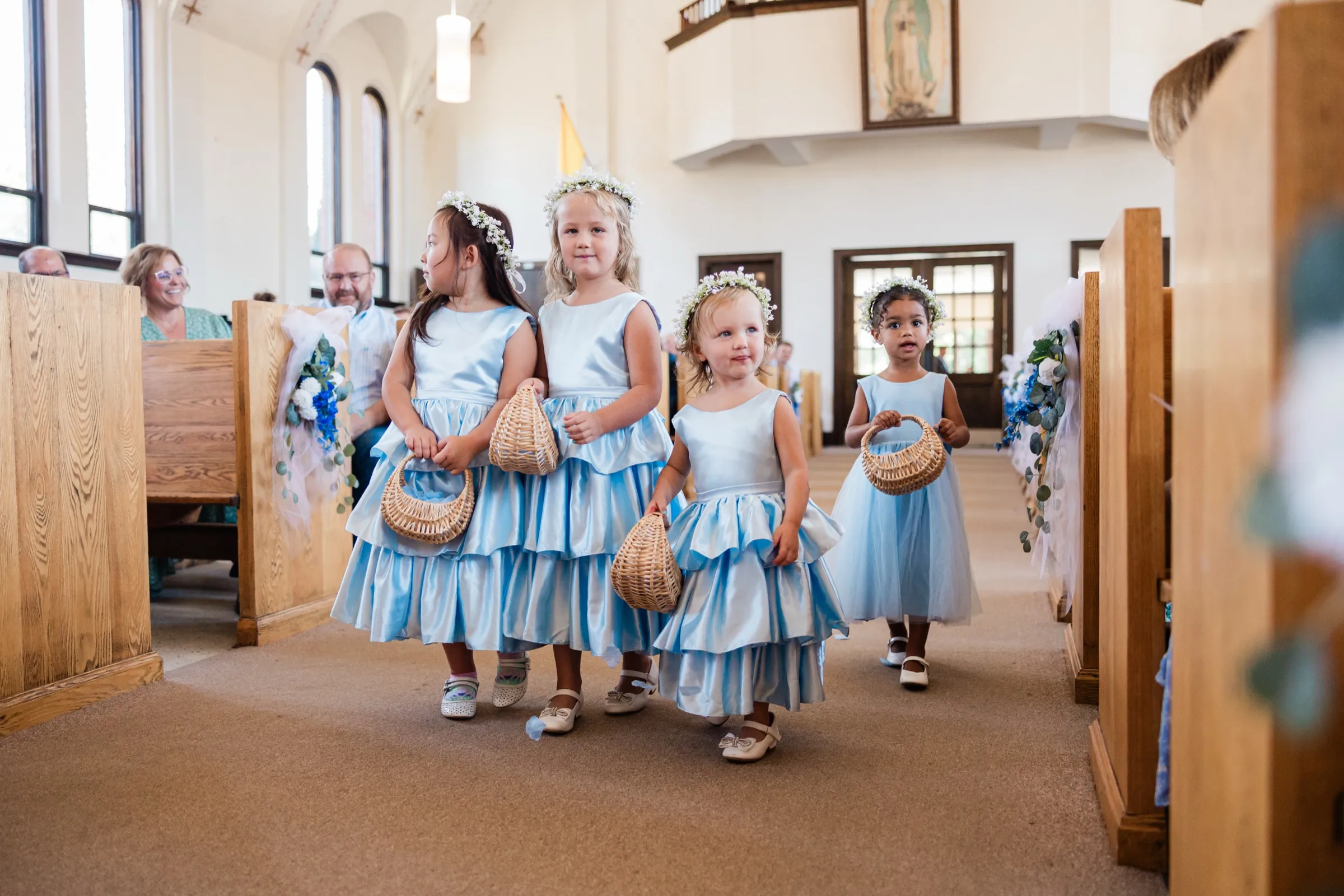 Four young flower girls in pale blue dresses and baby's breath crowns walk up the church aisle carrying woven baskets — Tim Larsen Photography, Brainerd Lakes MN
