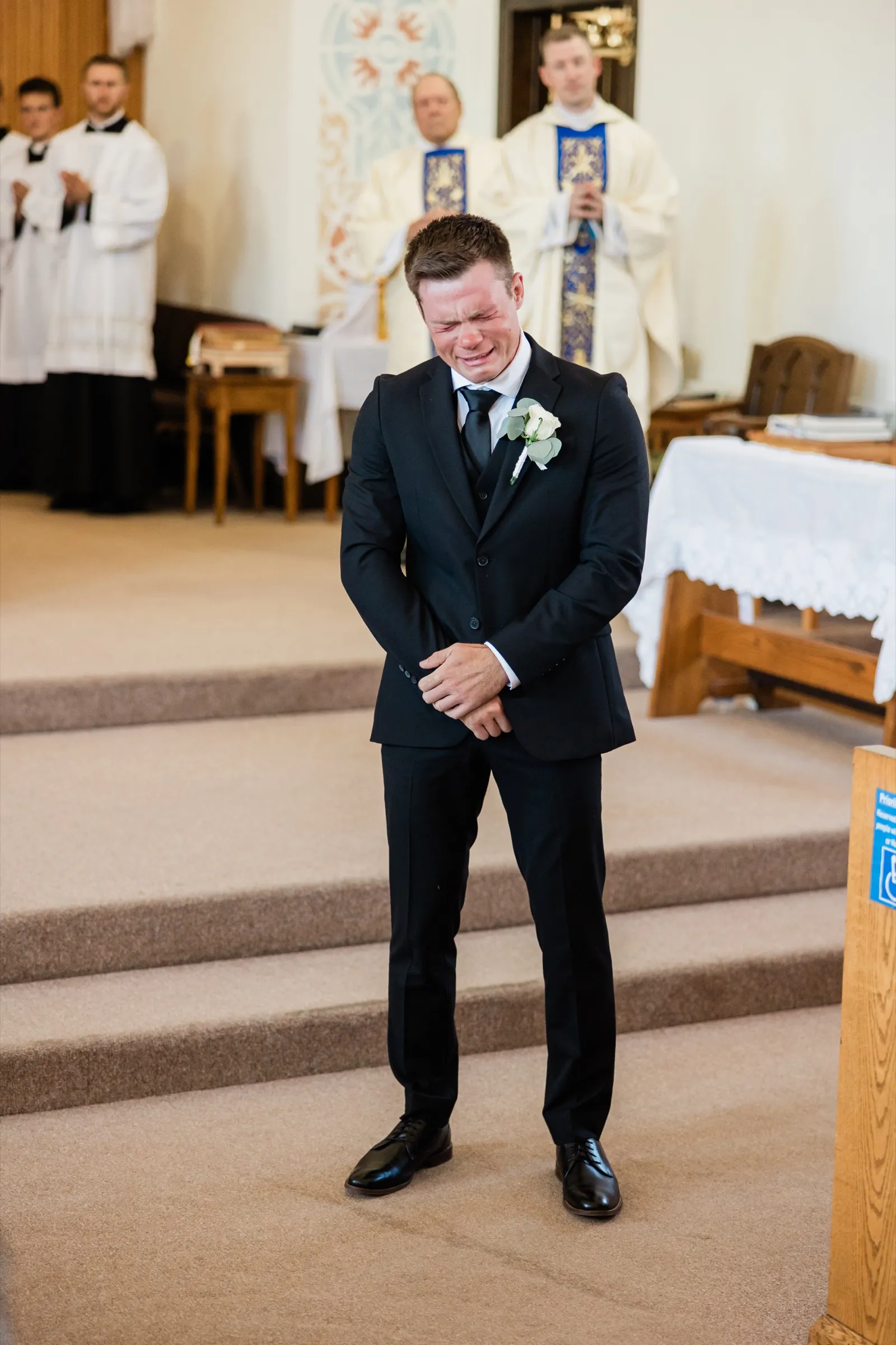 The groom doubles over crying on the altar steps of St. Joseph's Catholic Church in Crosby as the doors open for the bride's entrance — Tim Larsen Photography, Brainerd Lakes MN