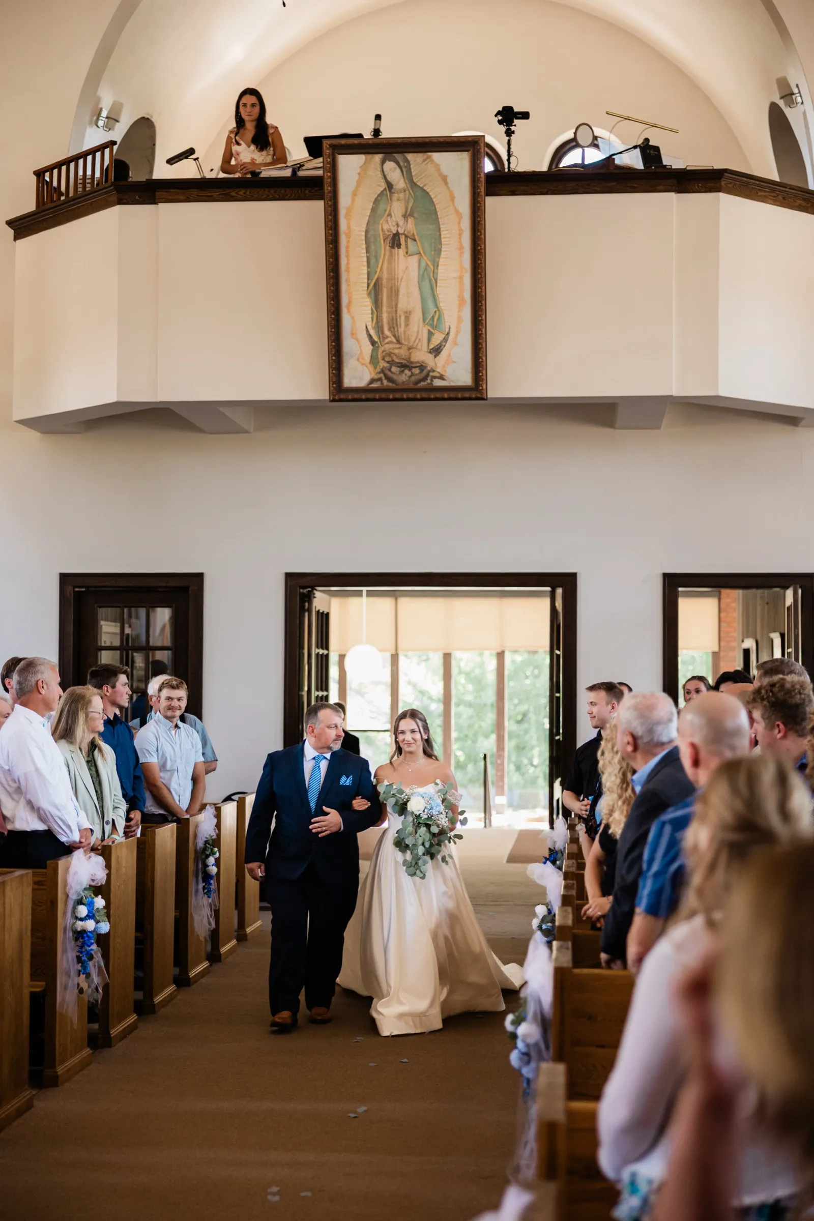 The bride enters St. Joseph's Catholic Church on her father's arm beneath a painting of Our Lady of Guadalupe — Tim Larsen Photography, Brainerd Lakes MN