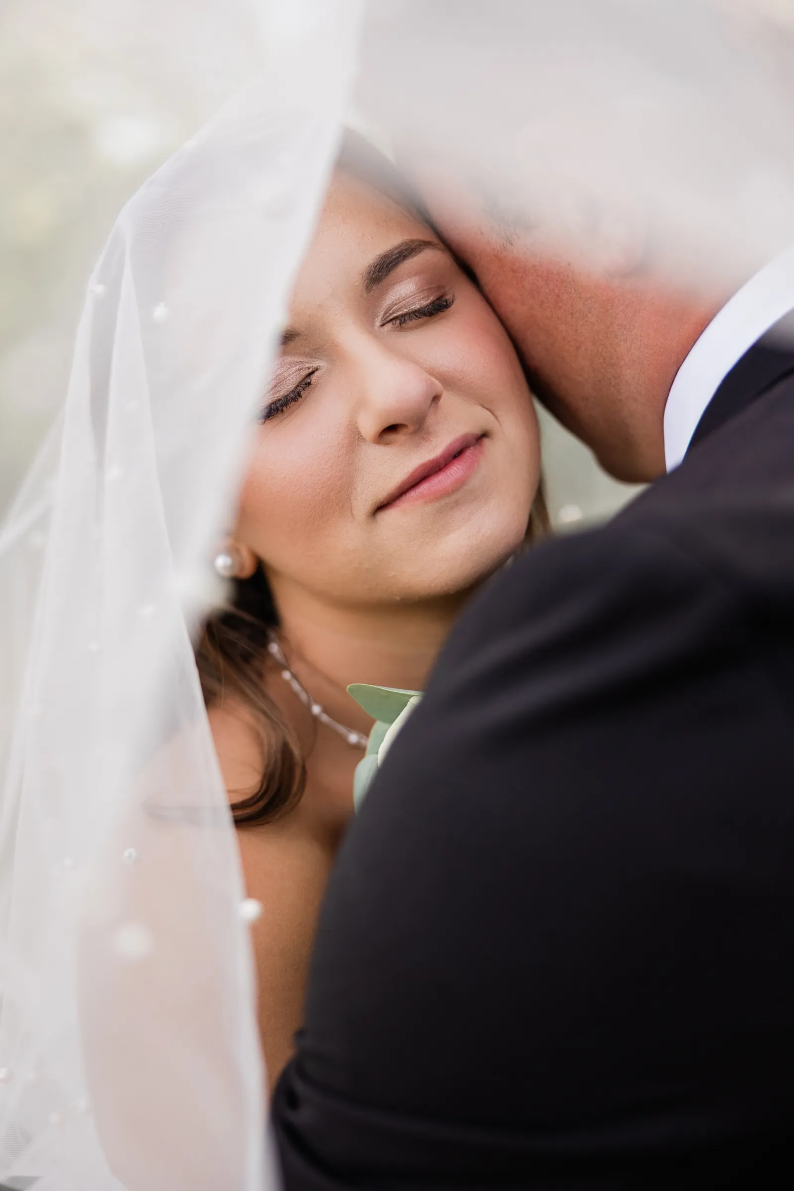 The bride rests her cheek against the groom's shoulder with her eyes closed, framed between the edge of her veil and his dark suit — Tim Larsen Photography, Brainerd Lakes MN