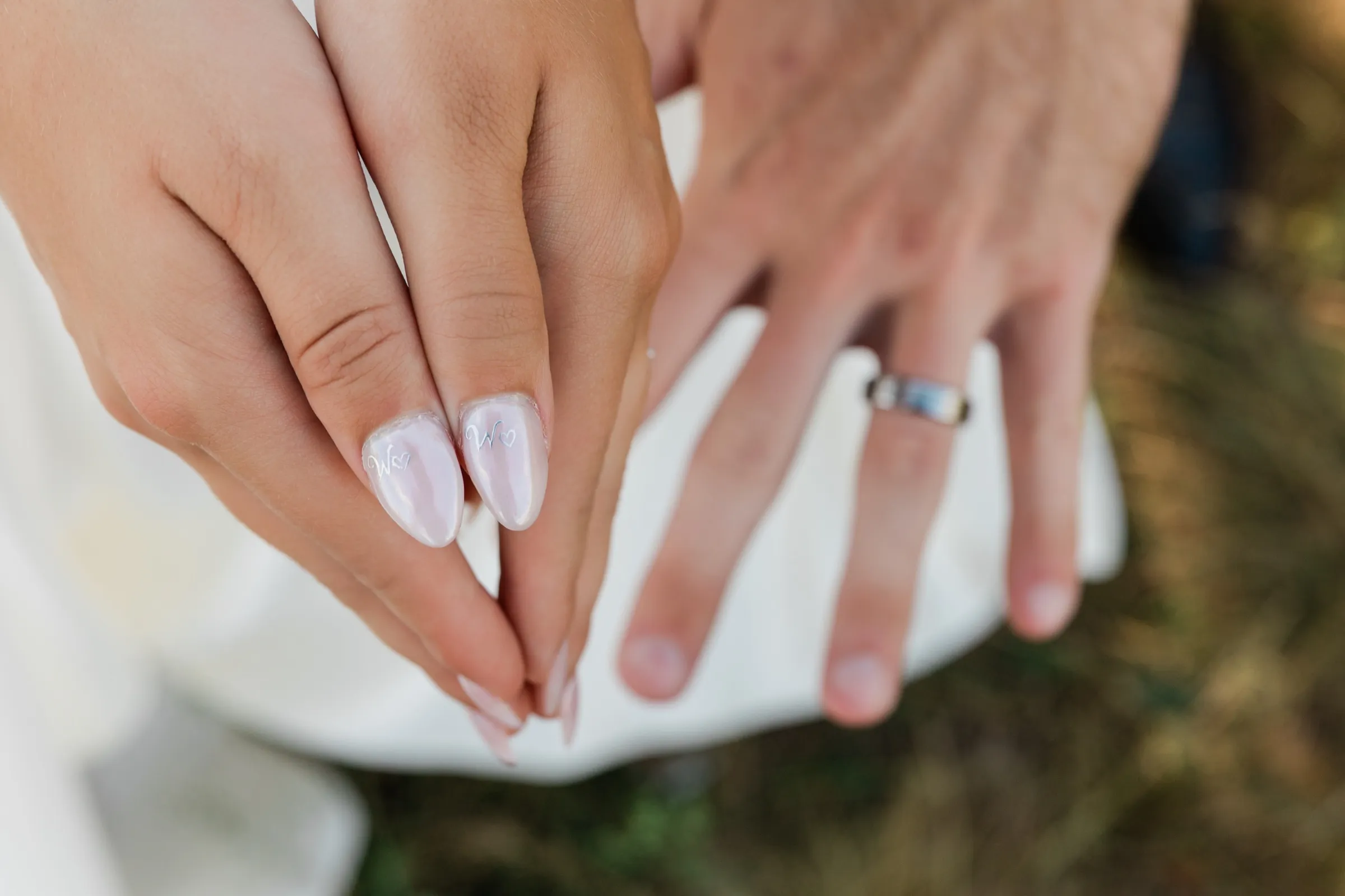 The bride and groom hold their hands out over her white skirt, showing her lettered nails and his dark wedding band — Tim Larsen Photography, Brainerd Lakes MN