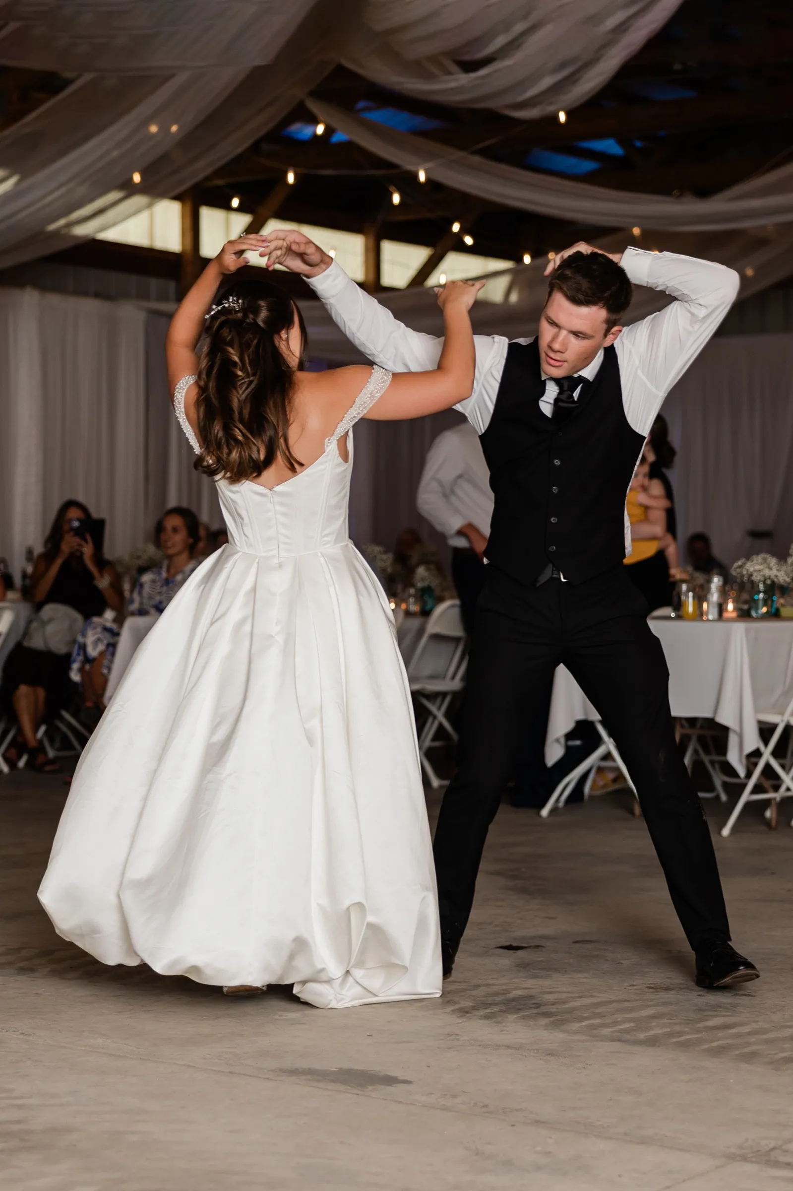 The groom raises his arms as the bride spins under them during their first dance in the draped reception hall — Tim Larsen Photography, Brainerd Lakes MN