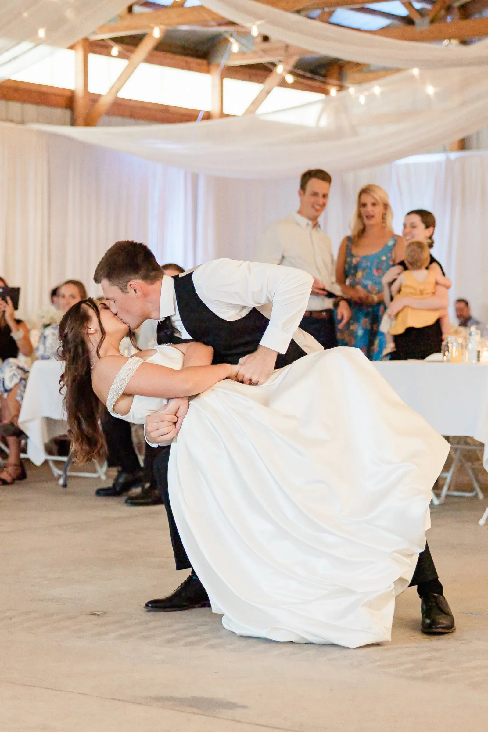 The groom dips the bride into a kiss at the end of their first dance while seated guests watch from the perimeter — Tim Larsen Photography, Brainerd Lakes MN