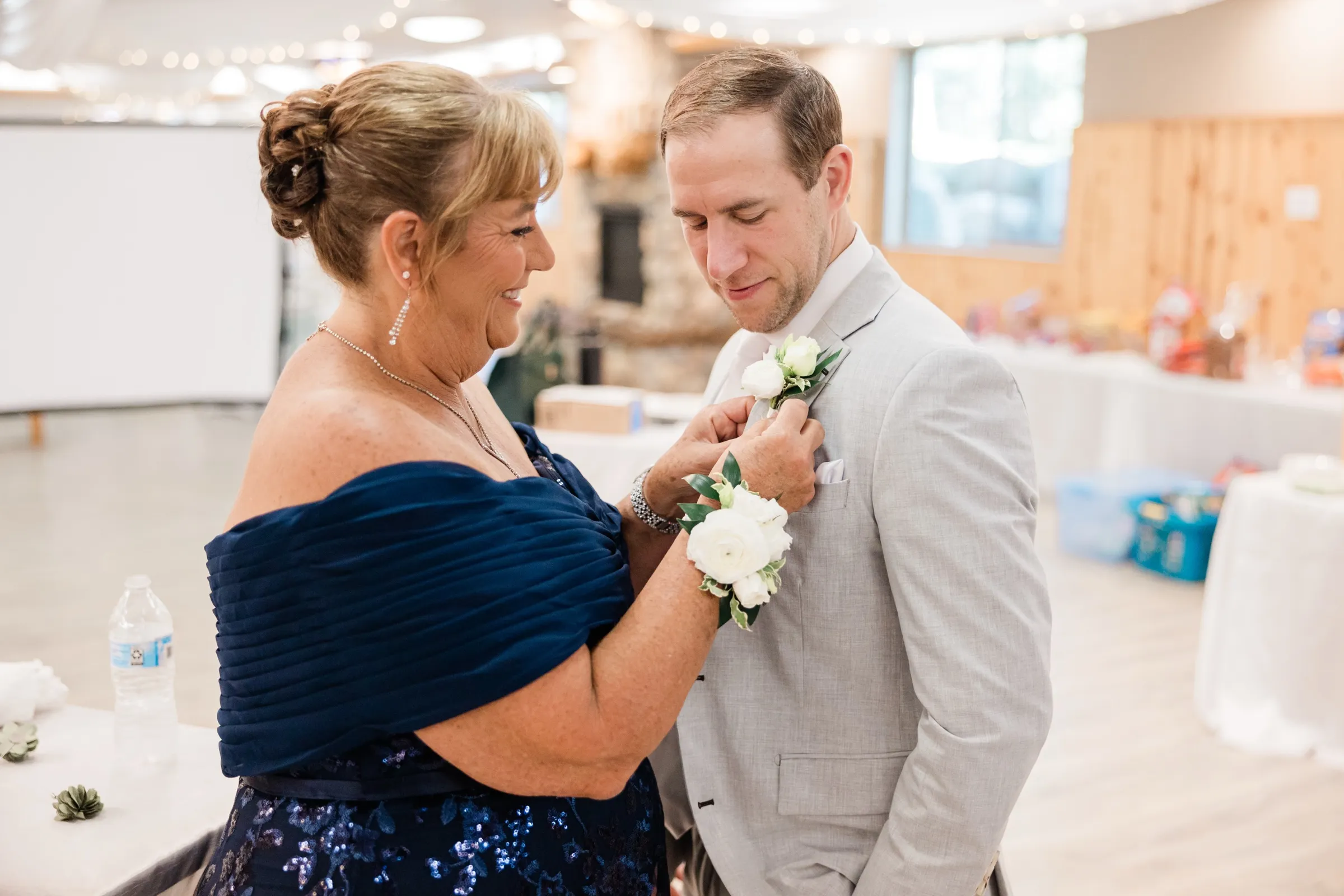 Alex looks down as his mother, in a navy dress and white wrist corsage, pins a white rose boutonniere to his light gray suit — Tim Larsen Photography, Brainerd Lakes MN