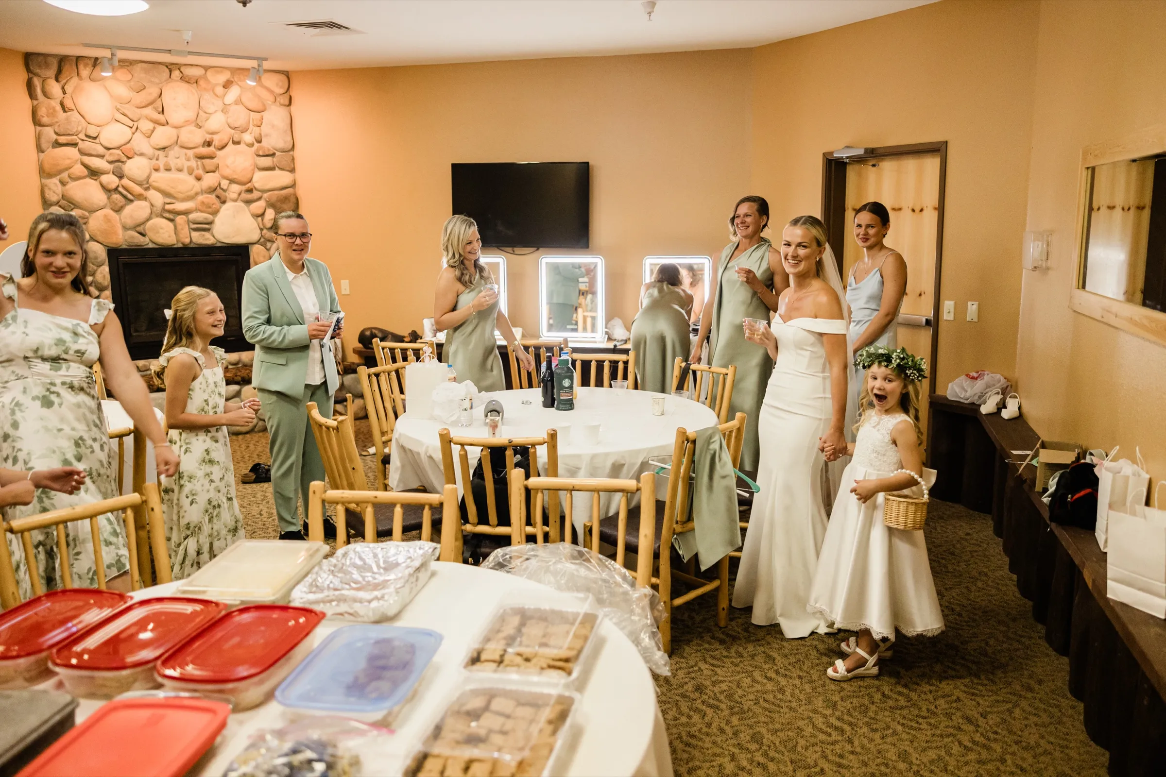 Josse stands with her bridal party and flower girl in a Whitefish Lodge getting-ready room with a stone fireplace, trays of homemade desserts filling the foreground table — Tim Larsen Photography, Brainerd Lakes MN